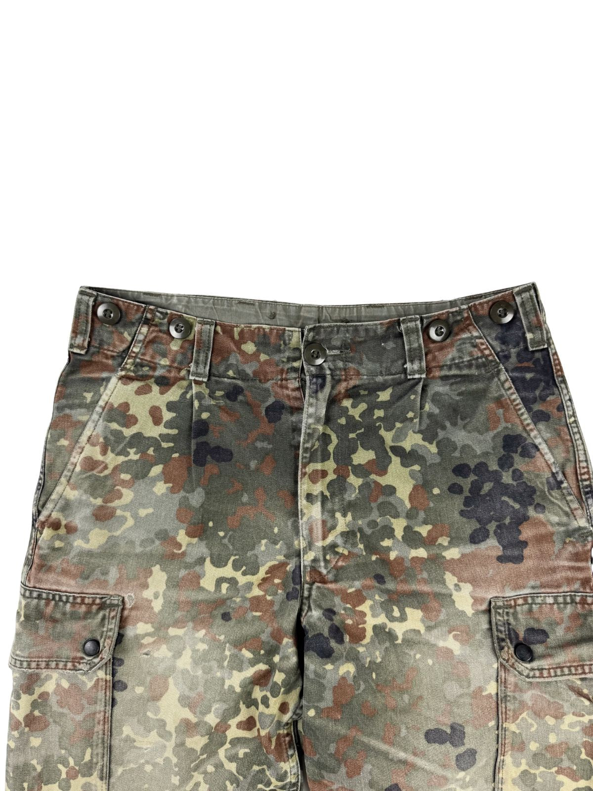 Detailansicht der vorderen Hüftpartie der Flecktarn-Hose. Gut erkennbar sind der Hosenbund mit Knöpfen für Hosenträger, Gürtelschlaufen, die Faltenlegung und die Ansätze der seitlichen Cargo-Taschen.