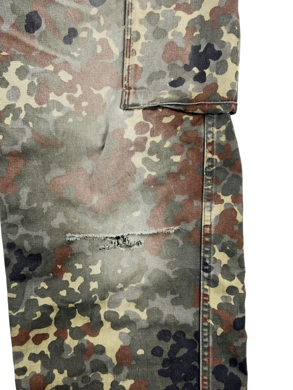 Detailansicht des linken Kniebereichs der Flecktarn-Hose mit einem horizontalen, leicht ausgefransten Riss im Stoff als authentisches Distressed-Merkmal.