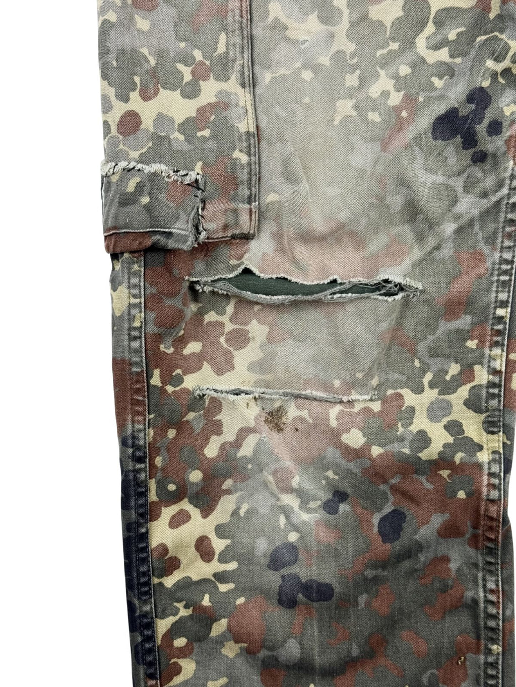 Detailaufnahme des rechten Hosenbeins im thrashed Look. Zu sehen sind zwei große, horizontale Risse direkt unter der Cargo-Tasche, die den Blick auf den grünen Taschenbeutel freigeben.
