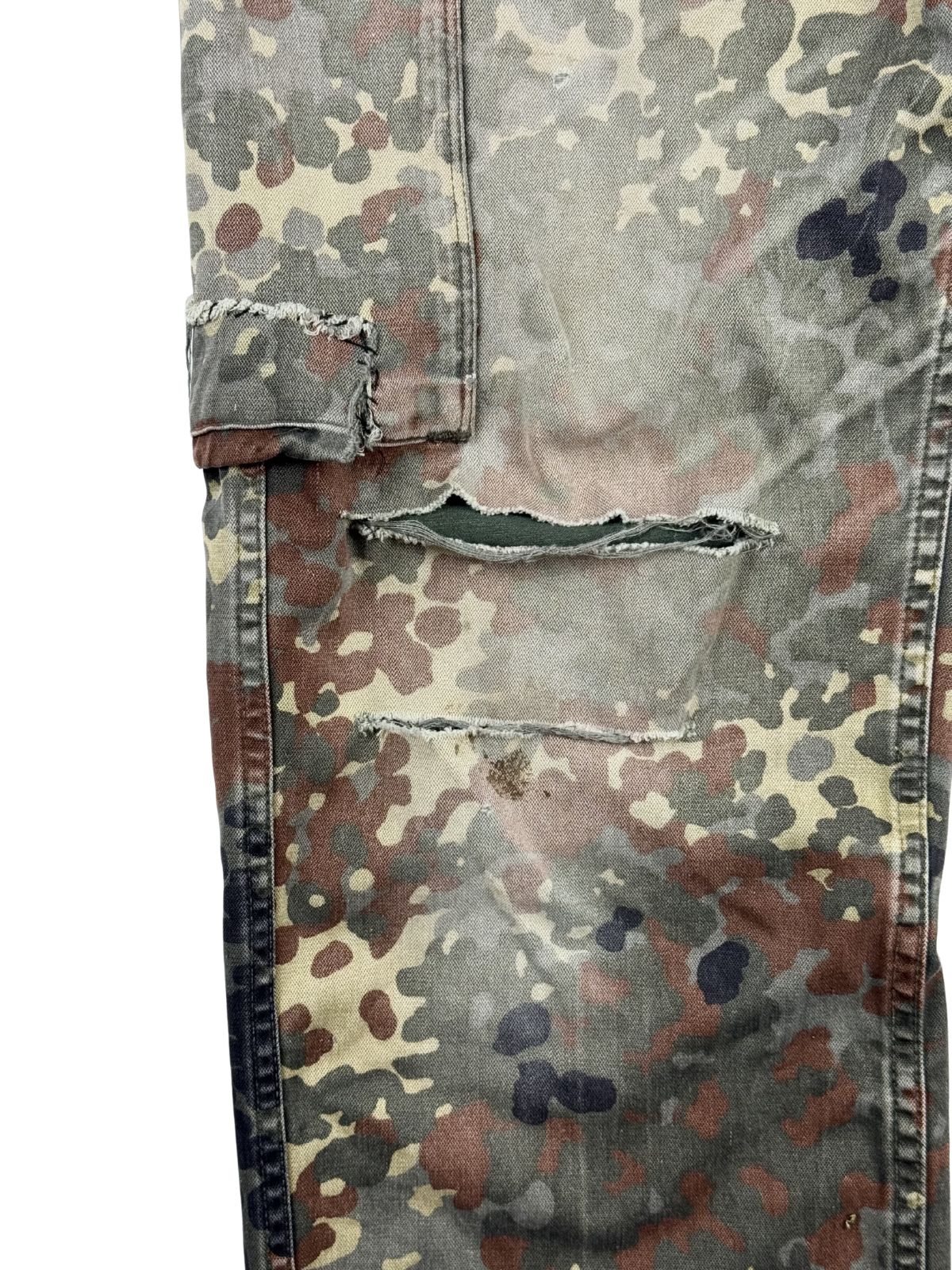 Detailaufnahme des rechten Hosenbeins im thrashed Look. Zu sehen sind zwei große, horizontale Risse direkt unter der Cargo-Tasche, die den Blick auf den grünen Taschenbeutel freigeben.