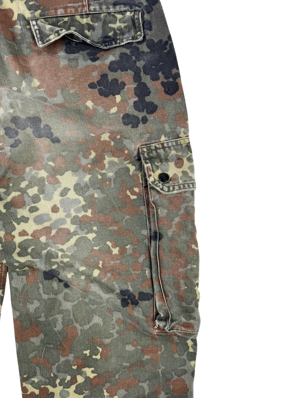 Detailaufnahme der seitlichen, aufgesetzten Cargo-Beintasche im Flecktarn-Muster, verschließbar mit einem verdeckten Druckknopf.