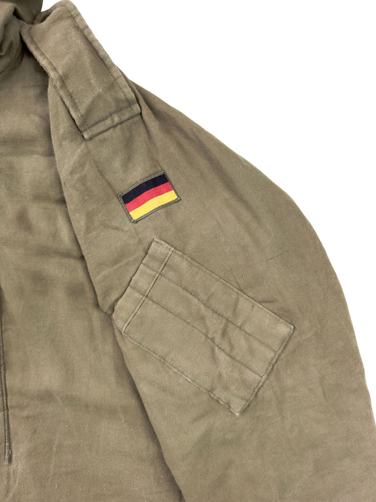 Detailaufnahme des linken Oberärmels mit einem aufgenähten schwarz-rot-goldenen Flaggen-Patch der Bundeswehr und einer darunter liegenden, aufgesetzten kleinen Ärmeltasche mit Stiftefächern.