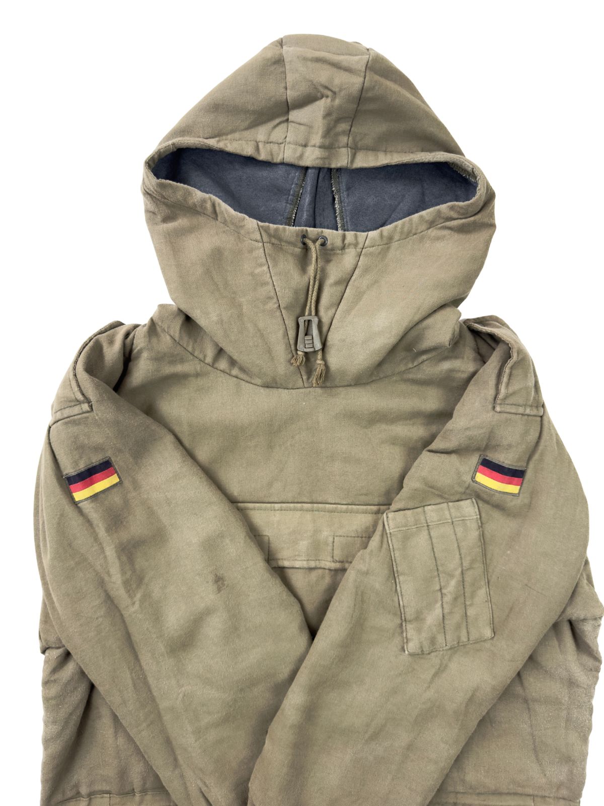 Nahaufnahme des oberen Bereichs im Flatlay mit verschränkten Ärmeln. Auf beiden Oberärmeln des olivfarbenen Bundeswehr-Smocks ist die deutsche Nationalflagge als gewebter Patch aufgenäht.