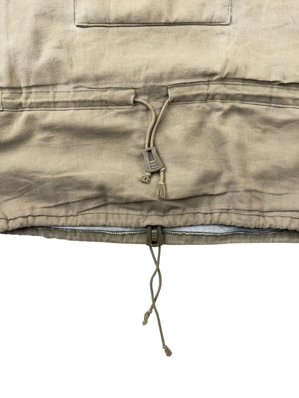 Detailansicht des unteren Bereichs des olivgrünen Vintage Bundeswehr Smocks. Zu sehen sind der verstellbare Kordelzug im Taillentunnel mit einem olivfarbenen Kunststoff-Stopper sowie ein weiterer Kordelzug direkt am unteren Saum des Anoraks.