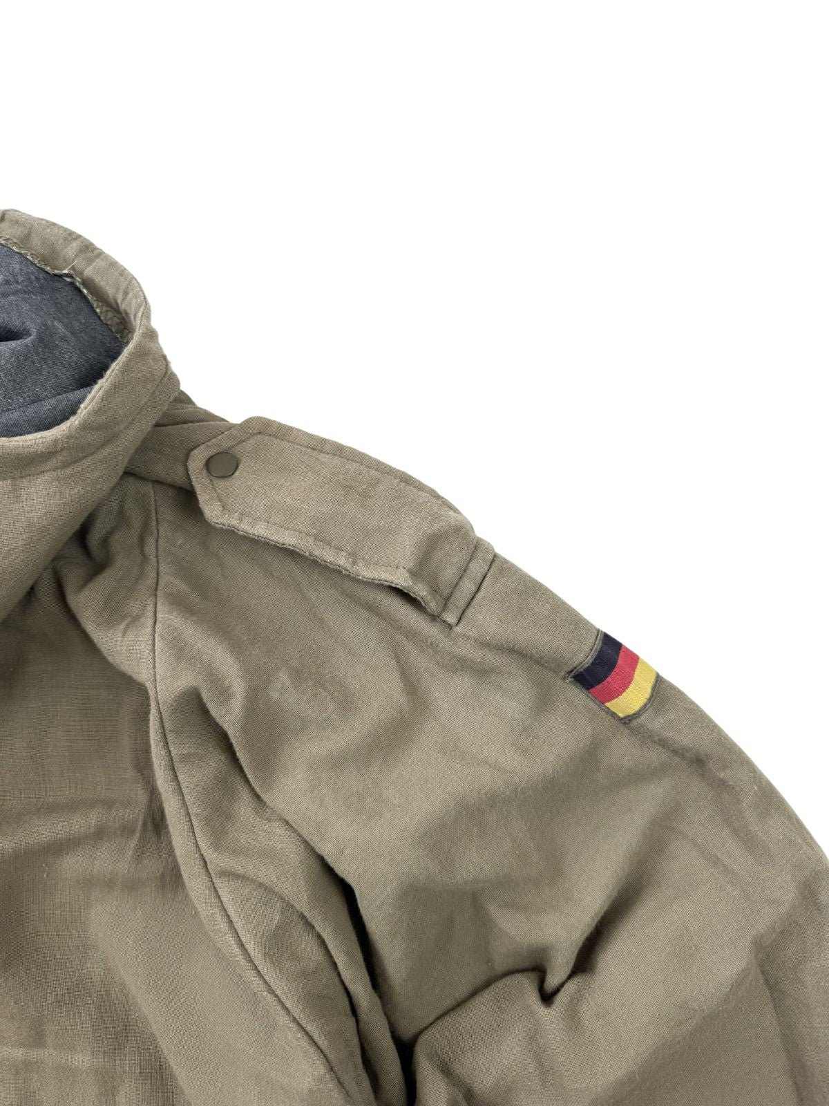 Nahaufnahme der rechten Schulterpartie des 80er-Jahre Smocks mit Fokus auf die Schulterklappe (Schlaufenschulterklappe) mit olivgrünem Metalldruckknopf und den angrenzenden Flaggen-Patch.
