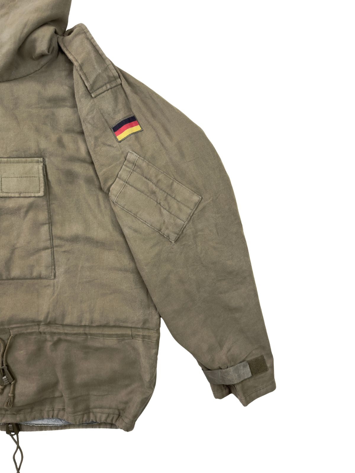 Seiten- und Ärmelansicht des Vintage-Militär-Smocks. Gezeigt werden die Schulterklappe mit Druckknopf, der deutsche Flaggen-Patch sowie der Ärmelbund mit Klettverschluss zur Weitenregulierung.