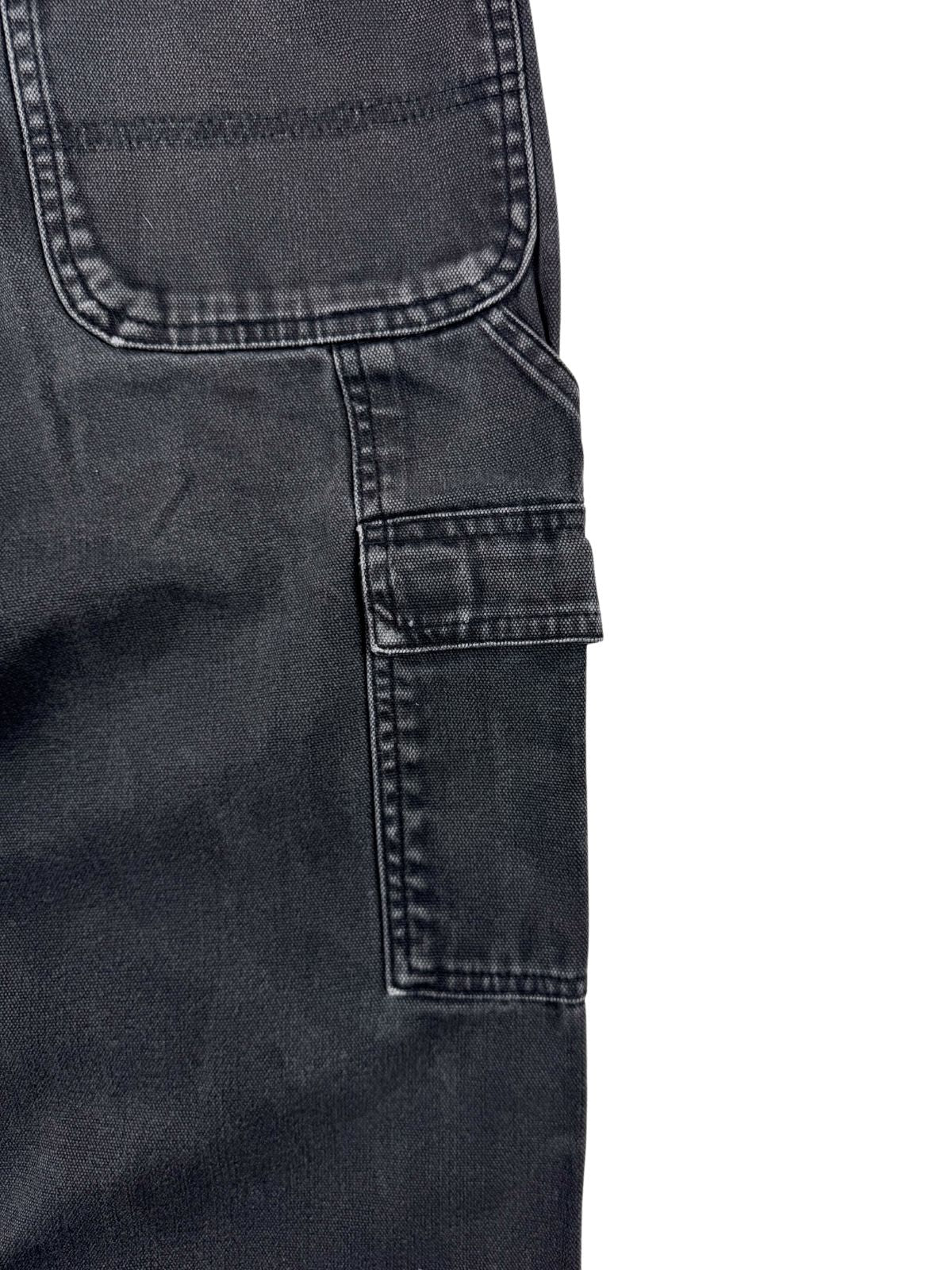 Nahaufnahme der rechten Oberschenkelseite einer schwarzen Dickies Carpenter Hose mit Fokus auf die aufgesetzte Werkzeugtasche (Utility Pocket) unterhalb der Gesäßtasche.