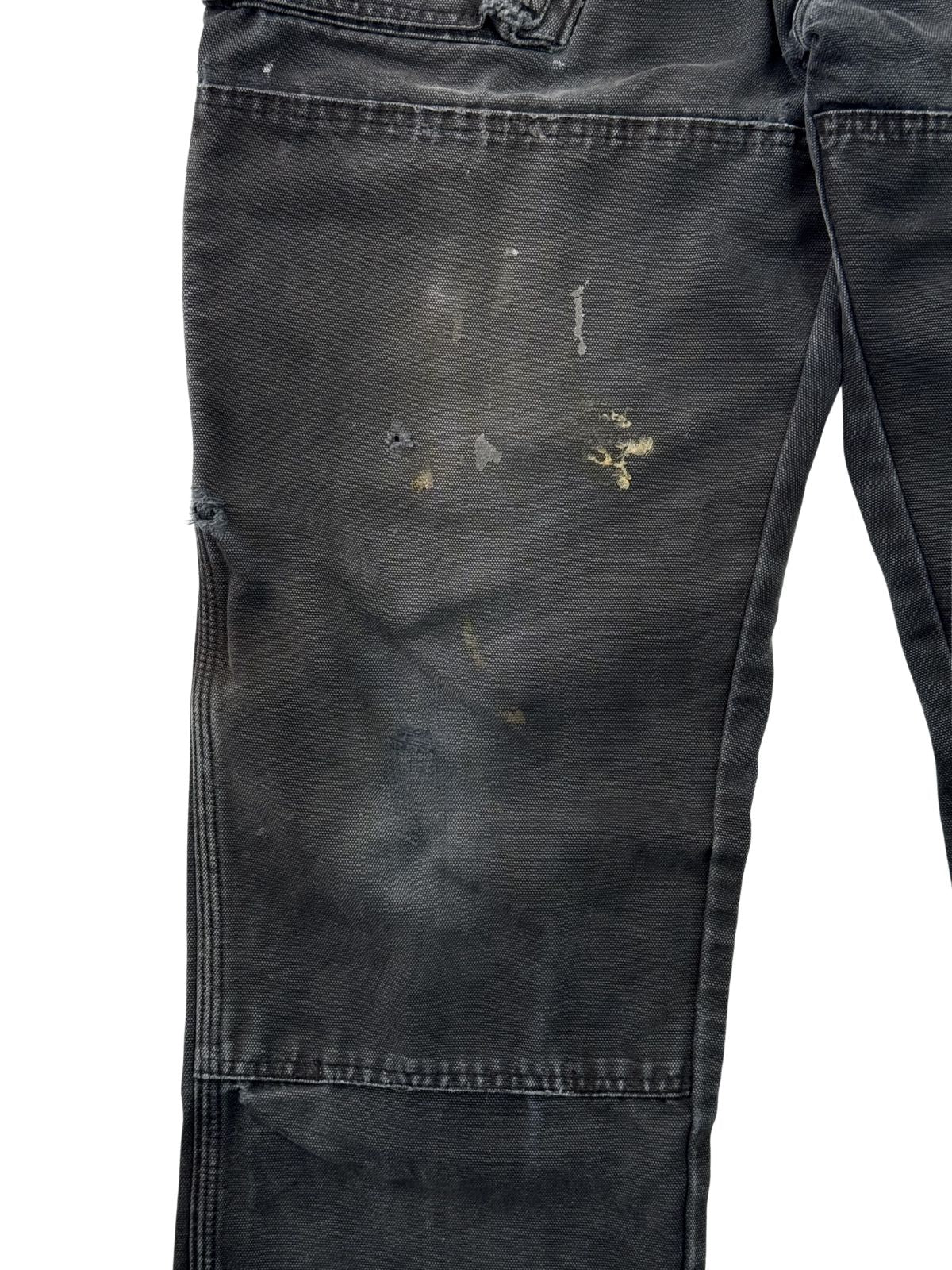 Detailaufnahme von Farbflecken und authentischen Verschmutzungen auf dem schwarzen Canvas-Stoff einer Vintage Workwear Hose.