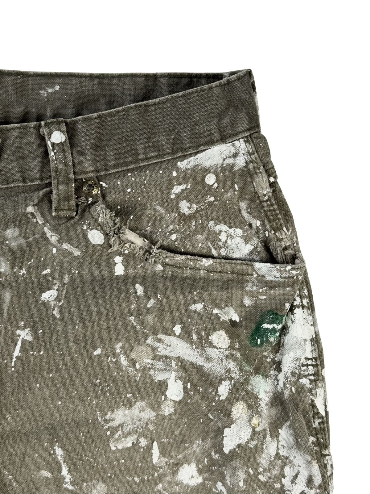 Detailaufnahme der linken vorderen Tasche. Der Taschenrand ist komplett zerschlissen (thrashed) und der umliegende Stoff zeigt Farbanhaftungen sowie einen kleinen grünen Farbfleck.
