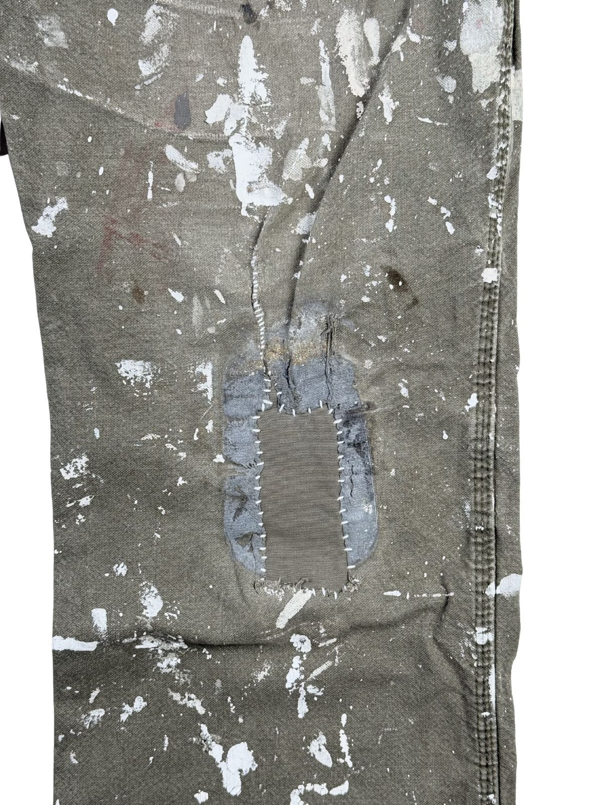 Detaillierte Nahaufnahme einer aufwendigen Reparaturstelle (Hand-Repair) auf dem linken Hosenbein. Ein großer Riss wurde mit einem grauen Stoff-Flicken unterlegt und mit einer auffälligen, weißen Kontrast-Stopfnaht per Hand vernäht.