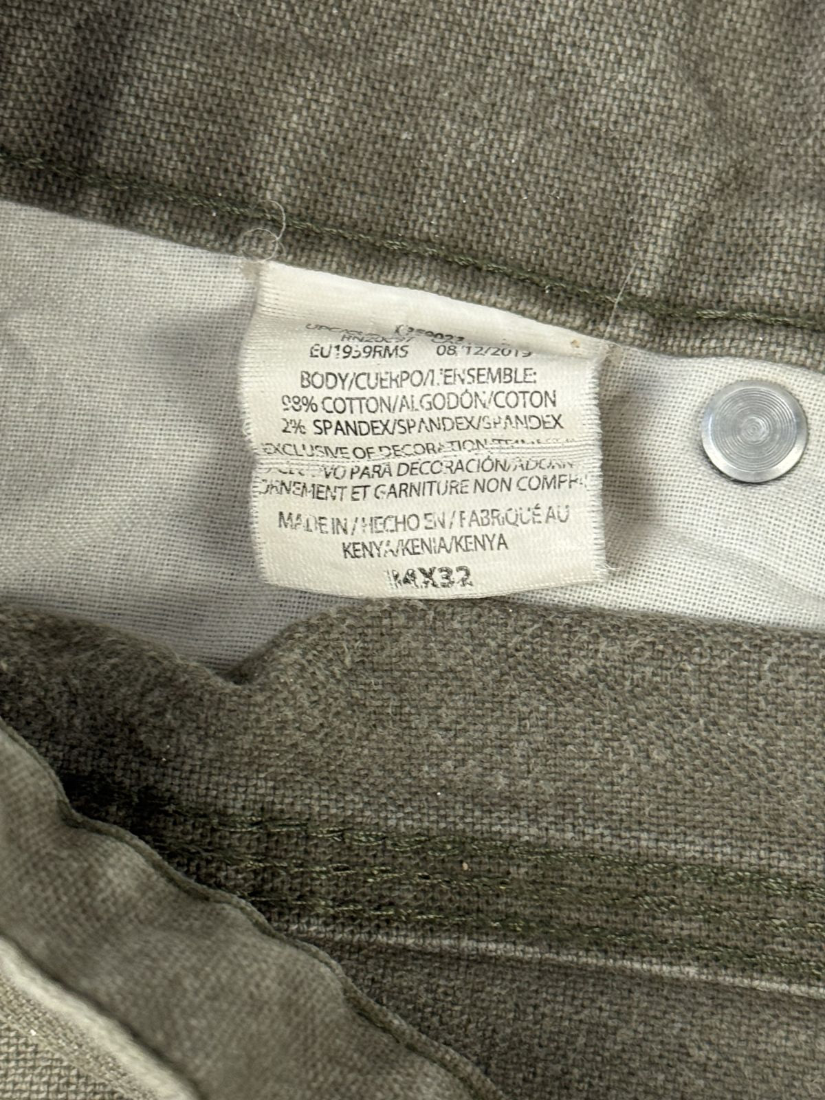 Makroaufnahme des originalen Stoffetiketts auf der Innenseite des Hosenbunds. Das weiße Label zeigt das Produktionsdatum 08/12/2019, die Materialzusammensetzung (98% Baumwolle, 2% Spandex), den Hinweis „Made in Kenya“ und die amerikanische Größe 34x32.