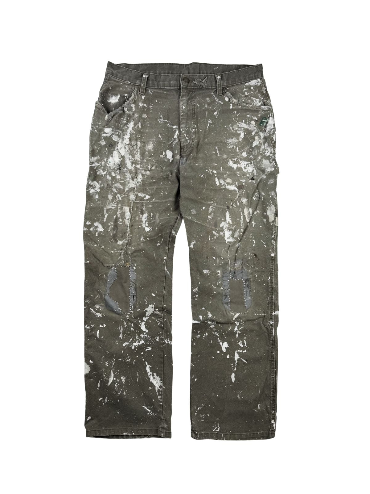 Komplettansicht der Vorderseite einer oliv-braunen Vintage Dickies Maler-Arbeitshose im Flatlay. Die Workwear-Hose zeigt extremen Distressed-Charakter mit intensiven weißen Farbspritzern und auffälligen, per Hand reparierten Flicken an beiden Knien. Flatlay auf weißem Hintergrund.