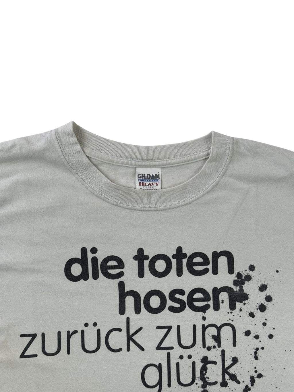 Nahaufnahme des Rundhalsausschnitts des grauen Toten-Hosen-Shirts. Der obere Teil des schwarzen Album-Schriftzugs und das weiße Nackenlabel sind am Kragen gut erkennbar.
