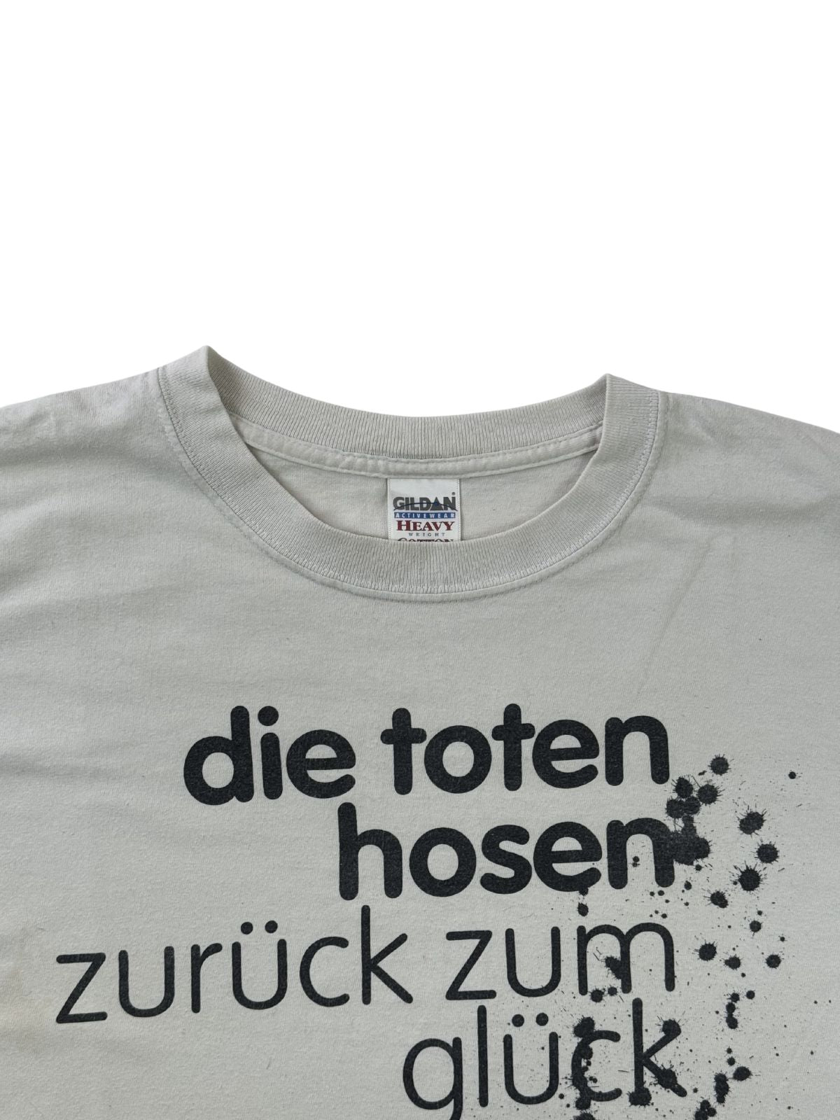 Nahaufnahme des Rundhalsausschnitts des grauen Toten-Hosen-Shirts. Der obere Teil des schwarzen Album-Schriftzugs und das weiße Nackenlabel sind am Kragen gut erkennbar.