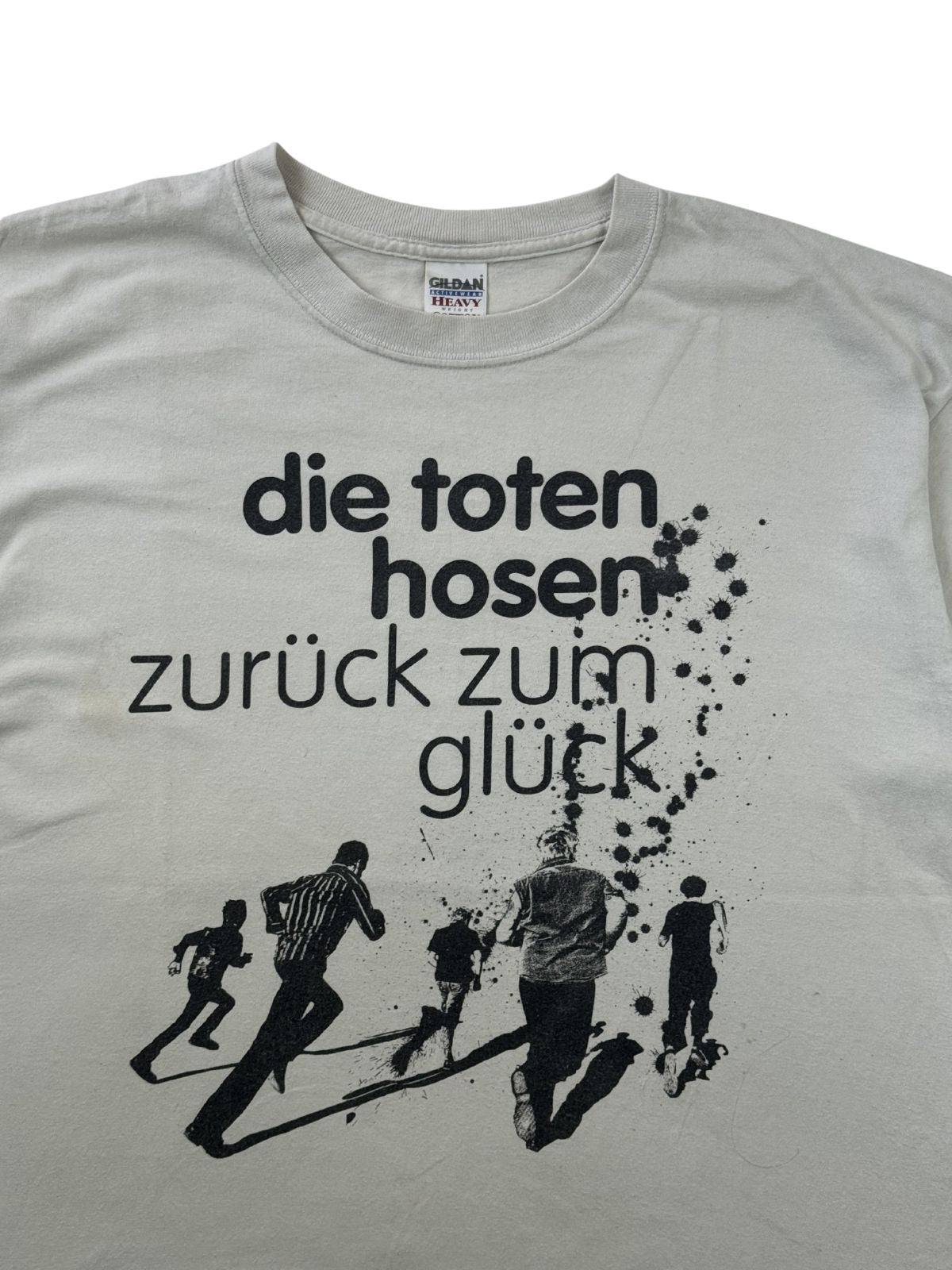 Detailansicht des vorderen Album-Prints. Zu sehen sind der schwarze Schriftzug „die toten hosen zurück zum glück“ mit Tinten- oder Farbspritzern sowie eine Grafik von fünf rennenden Personen im Siebdruck-Stil.