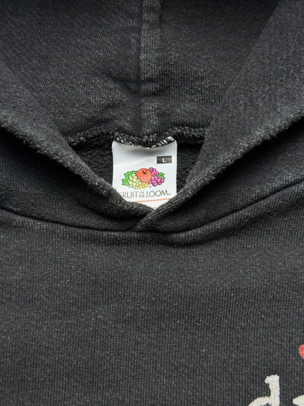 Nahaufnahme der Kapuzenbasis mit dem originalen weißen „Fruit of the Loom“-Nackenetikett in Größe L auf verwaschenem schwarzen Sweatstoff.