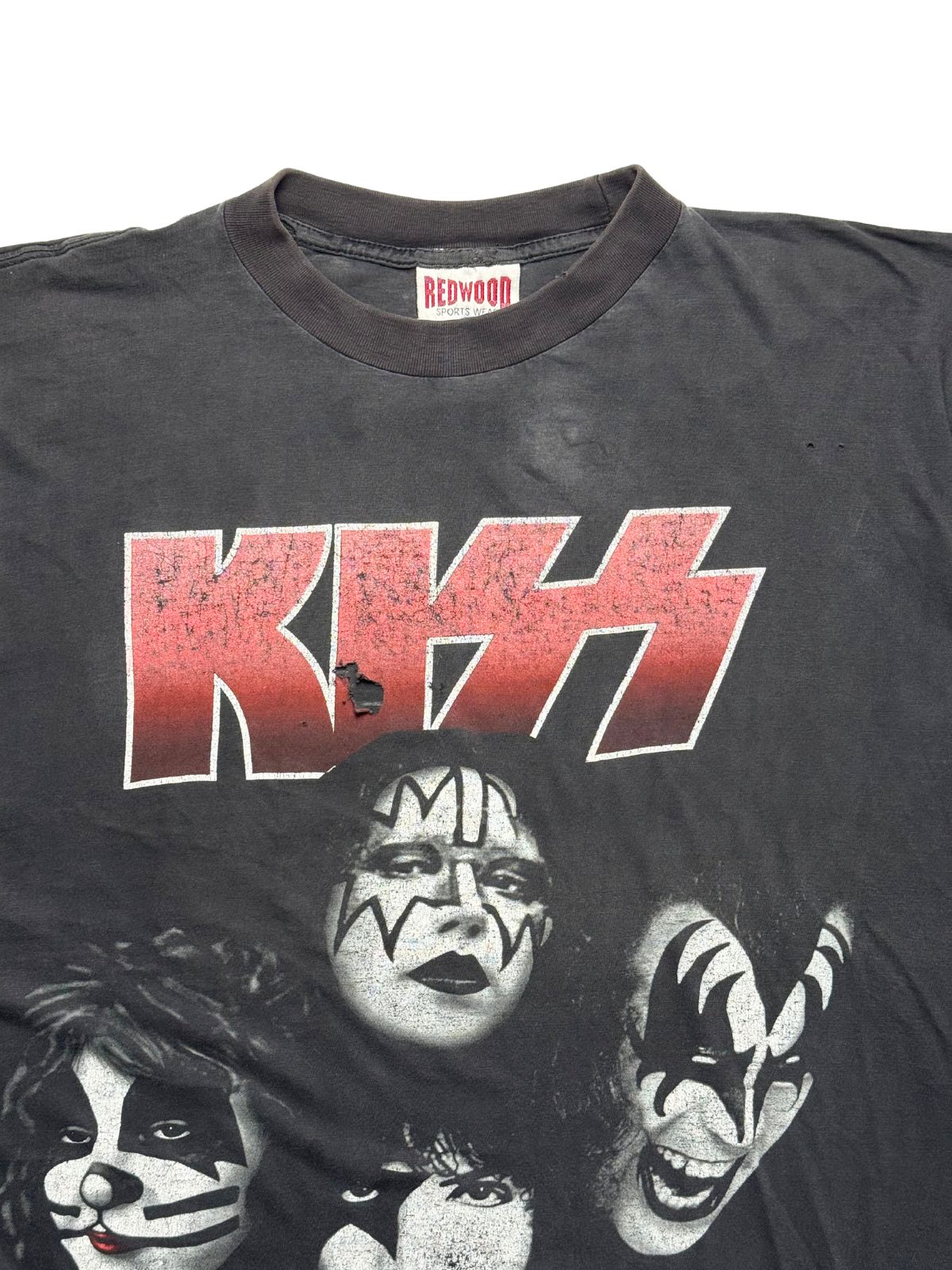 Detailansicht der vorderen Brustpartie mit geripptem Rundhalsausschnitt, dem rot-weißen KISS-Logo, Bandporträts und dem roten Redwood-Nackenetikett.