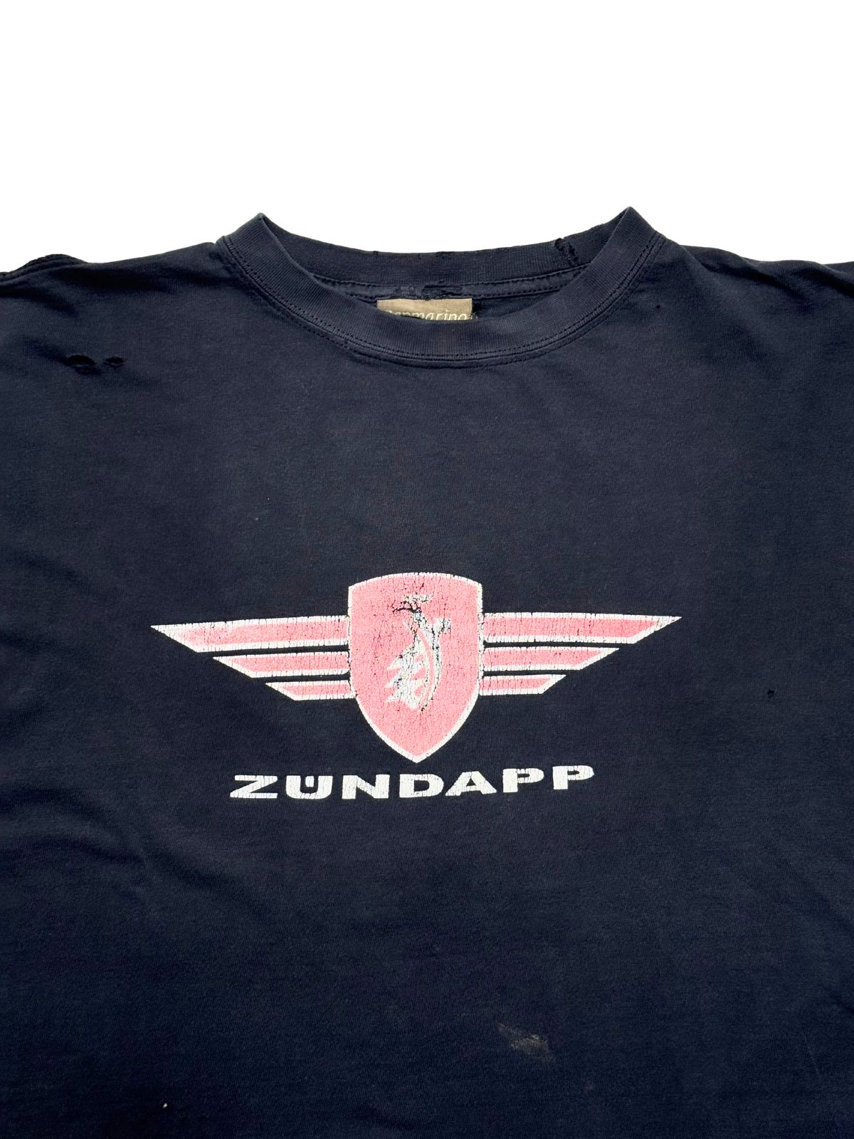 Detailansicht der vorderen Brustpartie mit geripptem Rundhalsausschnitt und dem rosa-weißen Zündapp-Wappen mit Flügeln.