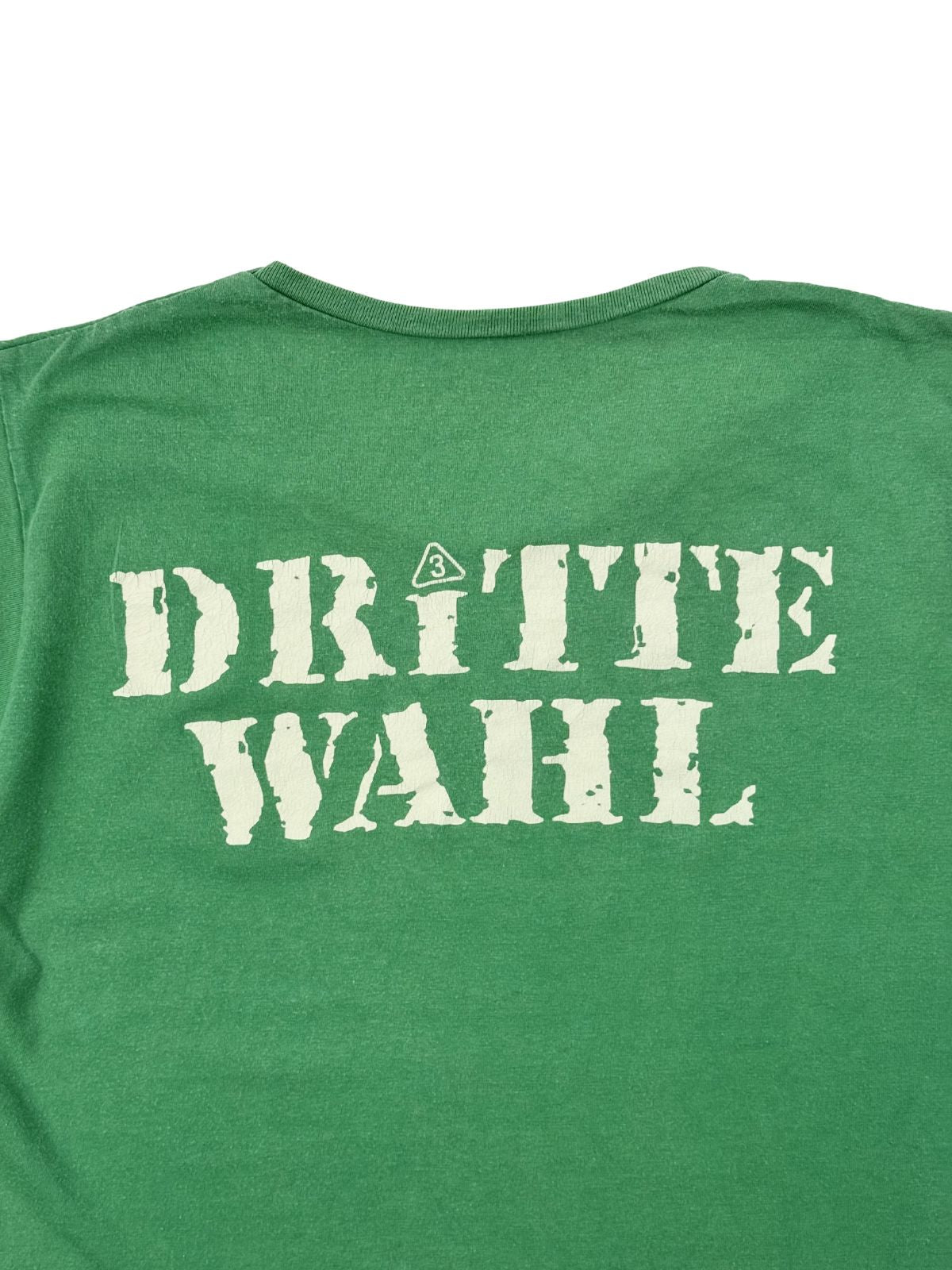 Nahaufnahme des rückseitigen Dritte Wahl Bandlogo-Siebdrucks auf dem grünen Baumwollstoff im distressed Vintage-Zustand.