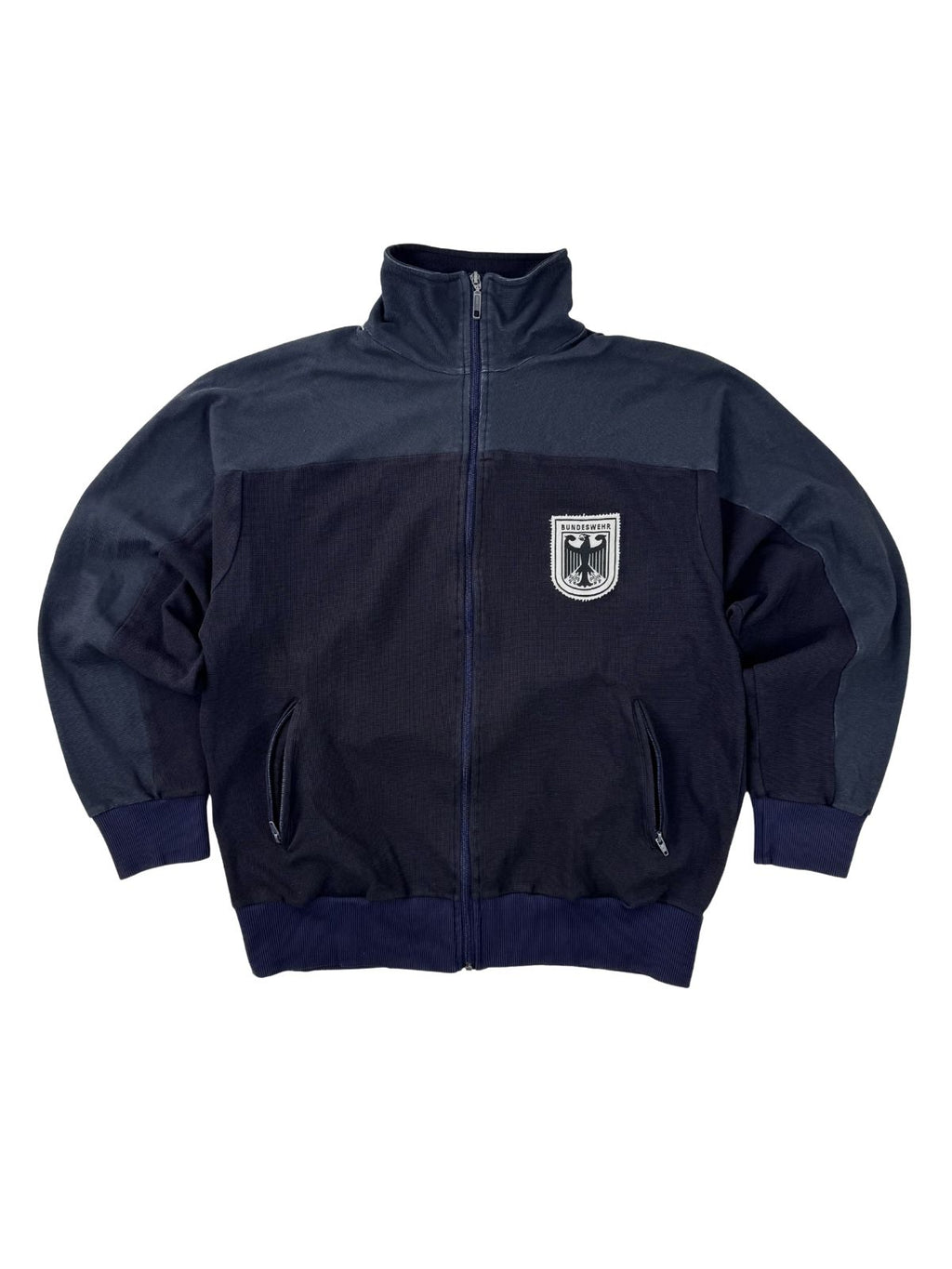 Vorderansicht einer dunkelblau eingefärbten Vintage Bundeswehr Trainingsjacke der 90er Jahre mit handgesticktem Bundesadler-Logo auf weißem Patch.
