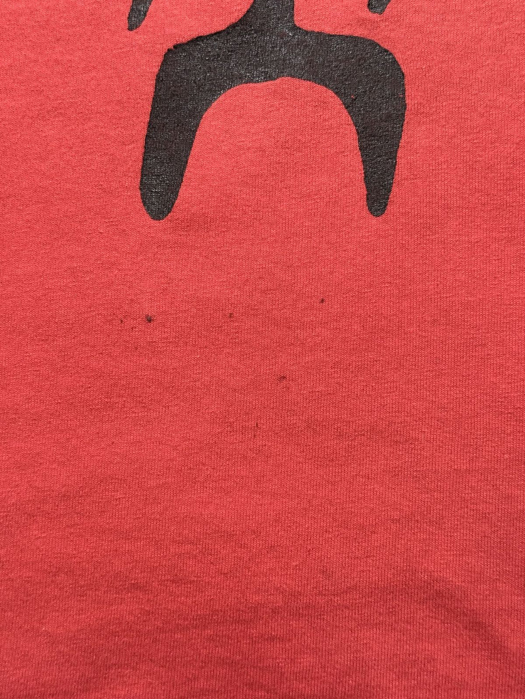 Makroaufnahme im Bereich unterhalb des Logos mit mehreren winzigen, dunklen Punkten/Flecken im Stoff.