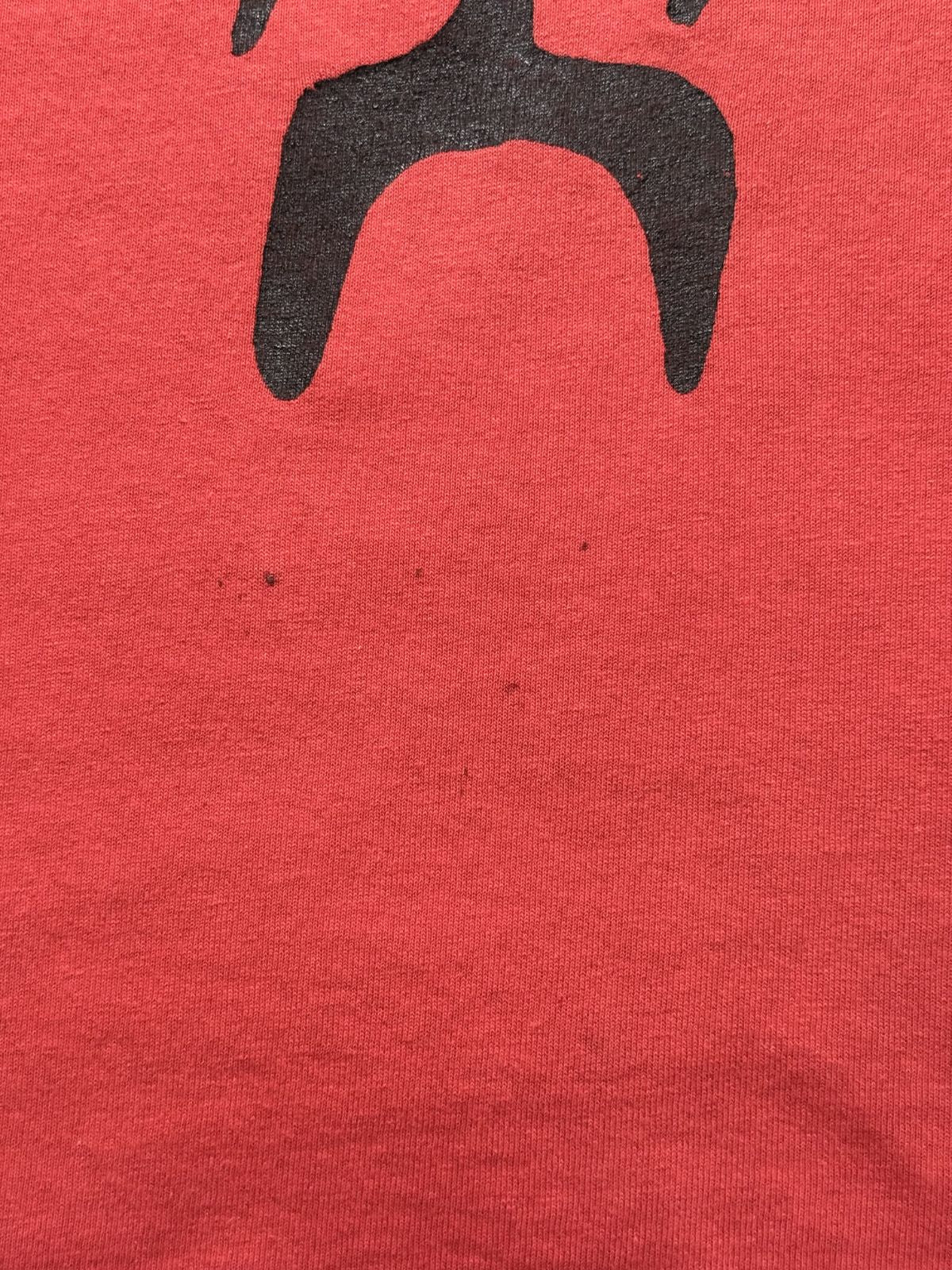 Makroaufnahme im Bereich unterhalb des Logos mit mehreren winzigen, dunklen Punkten/Flecken im Stoff.