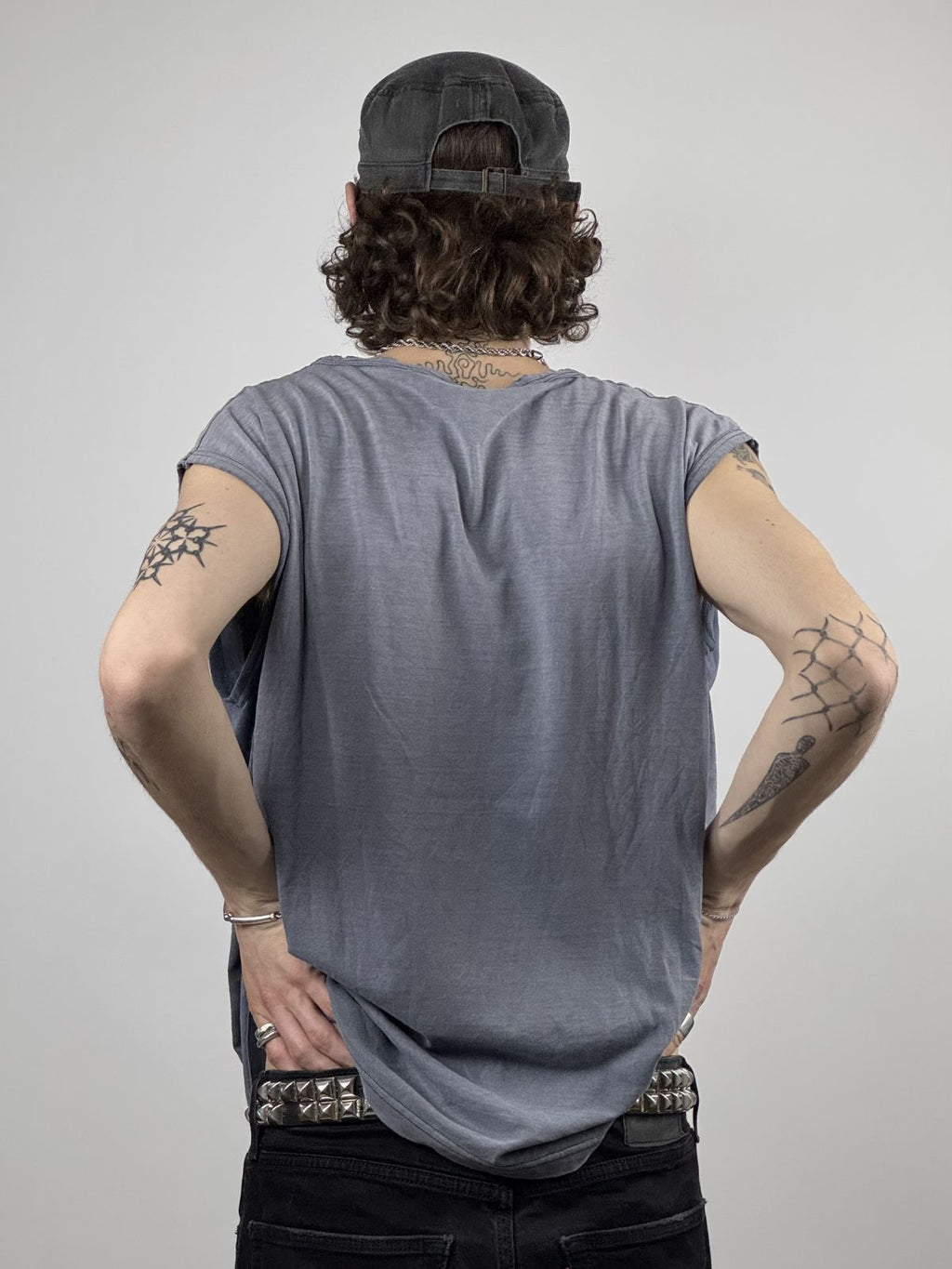Rückansicht des Modells im ärmellosen Shirt; verdeutlicht den weich fallenden Stoff und die Kombination mit einem Punk-Style Nietengürtel.