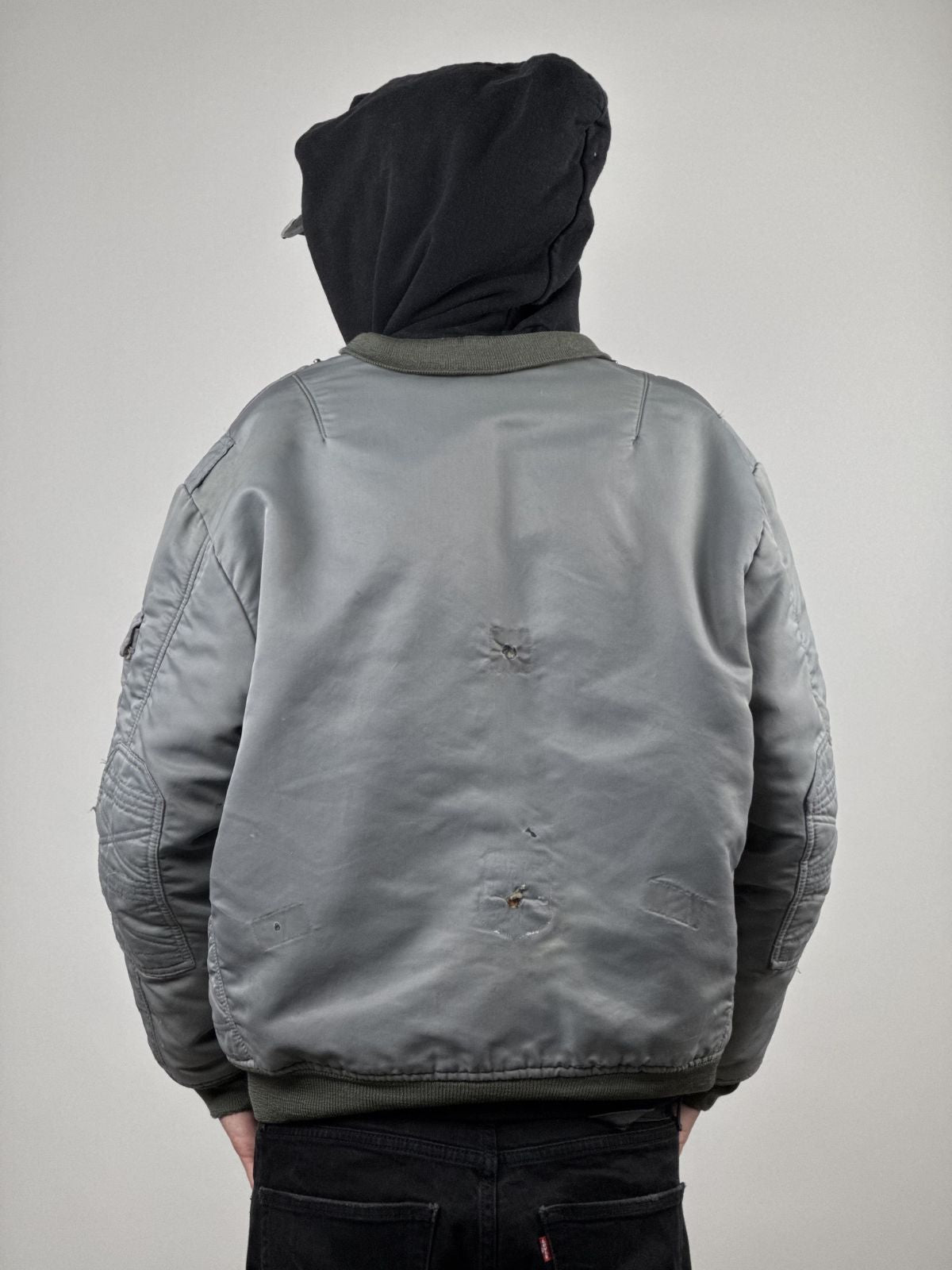 Rückansicht des Models in der verwaschenen Fliegerjacke; verdeutlicht die Platzierung der authentischen Löcher am Rücken und das markante Sun-Fading des Bundeswehr-Originals.