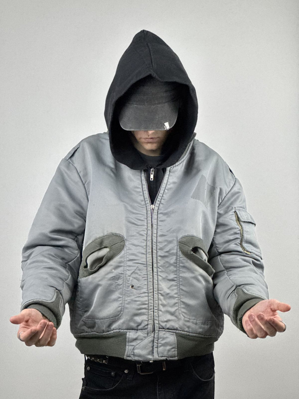 Frontale Lifestyle-Aufnahme eines Models in der distressed Bomberjacke; zeigt die voluminöse, boxy Passform und den kontrastreichen Look mit schwarzer Kapuze.
