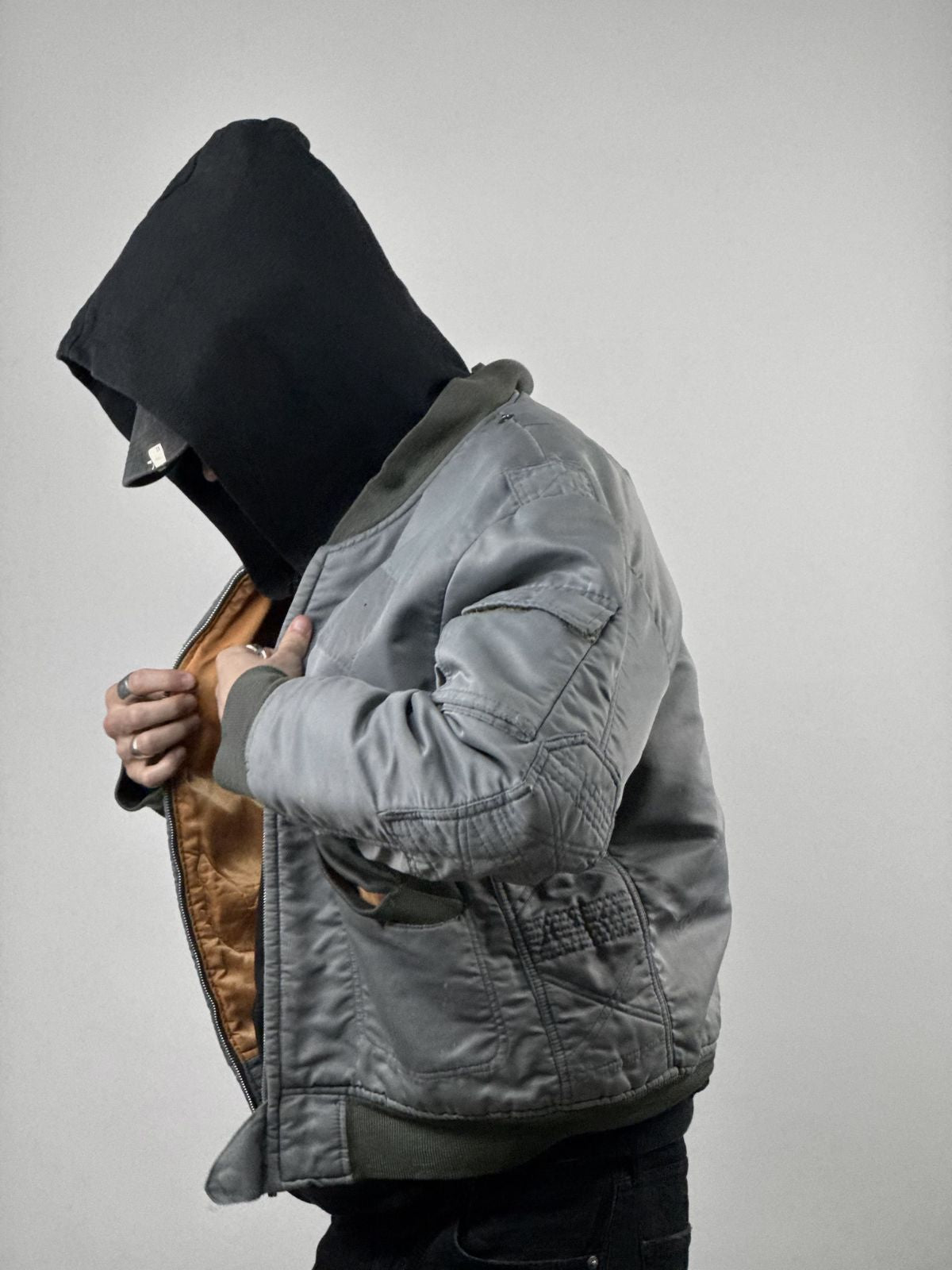 Seitenprofil des Models beim Öffnen der Jacke; zeigt das kontrastierende orangefarbene Innenfutter (Lining) und die robuste Textur der Vintage-Fliegerjacke.
