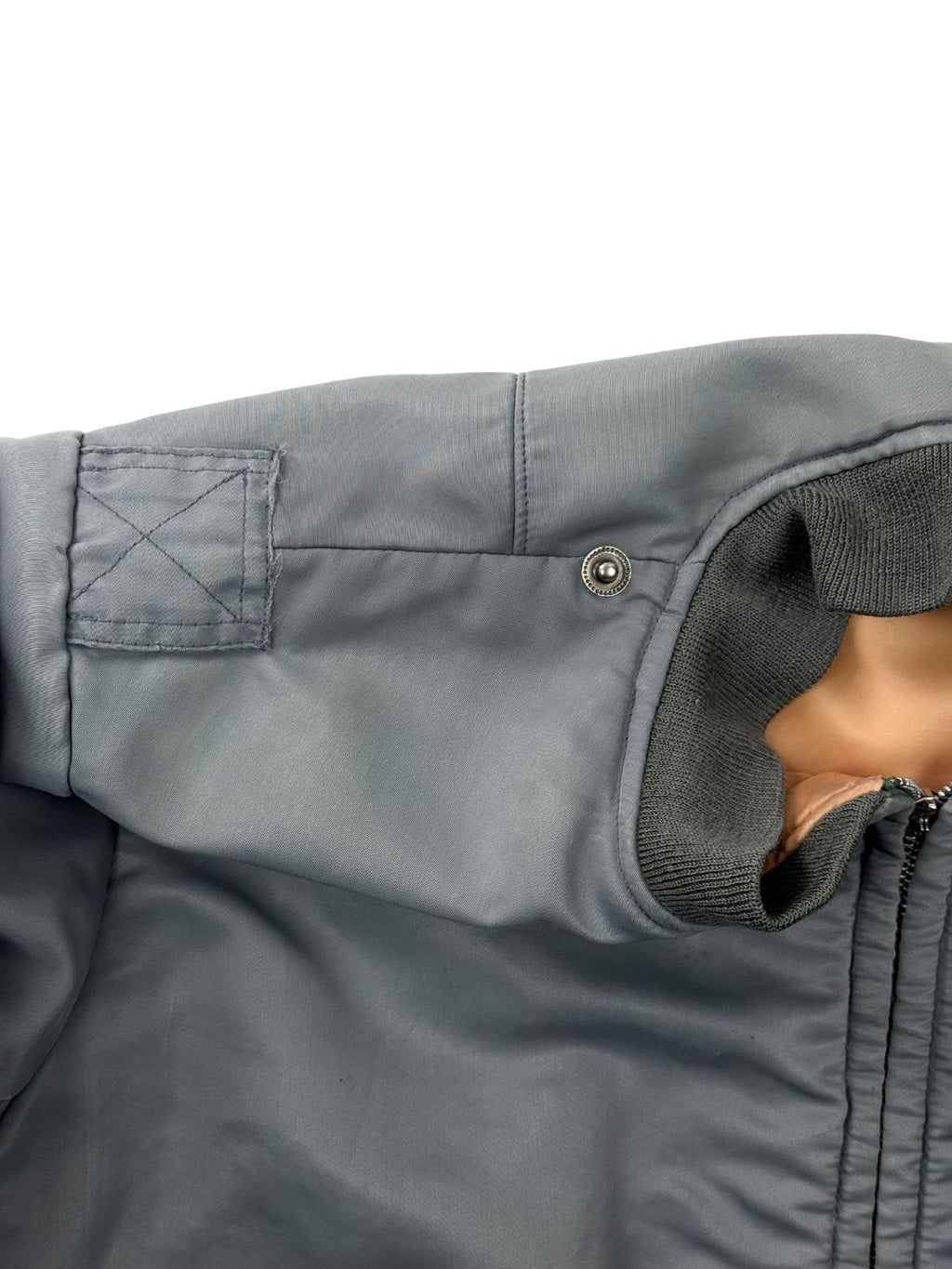 Nahaufnahme der rechten Schulterpartie; zeigt die markanten Nahtspuren und Verstärkungen einer entfernten Schulterklappe auf dem silbrig-blauen Nylon.