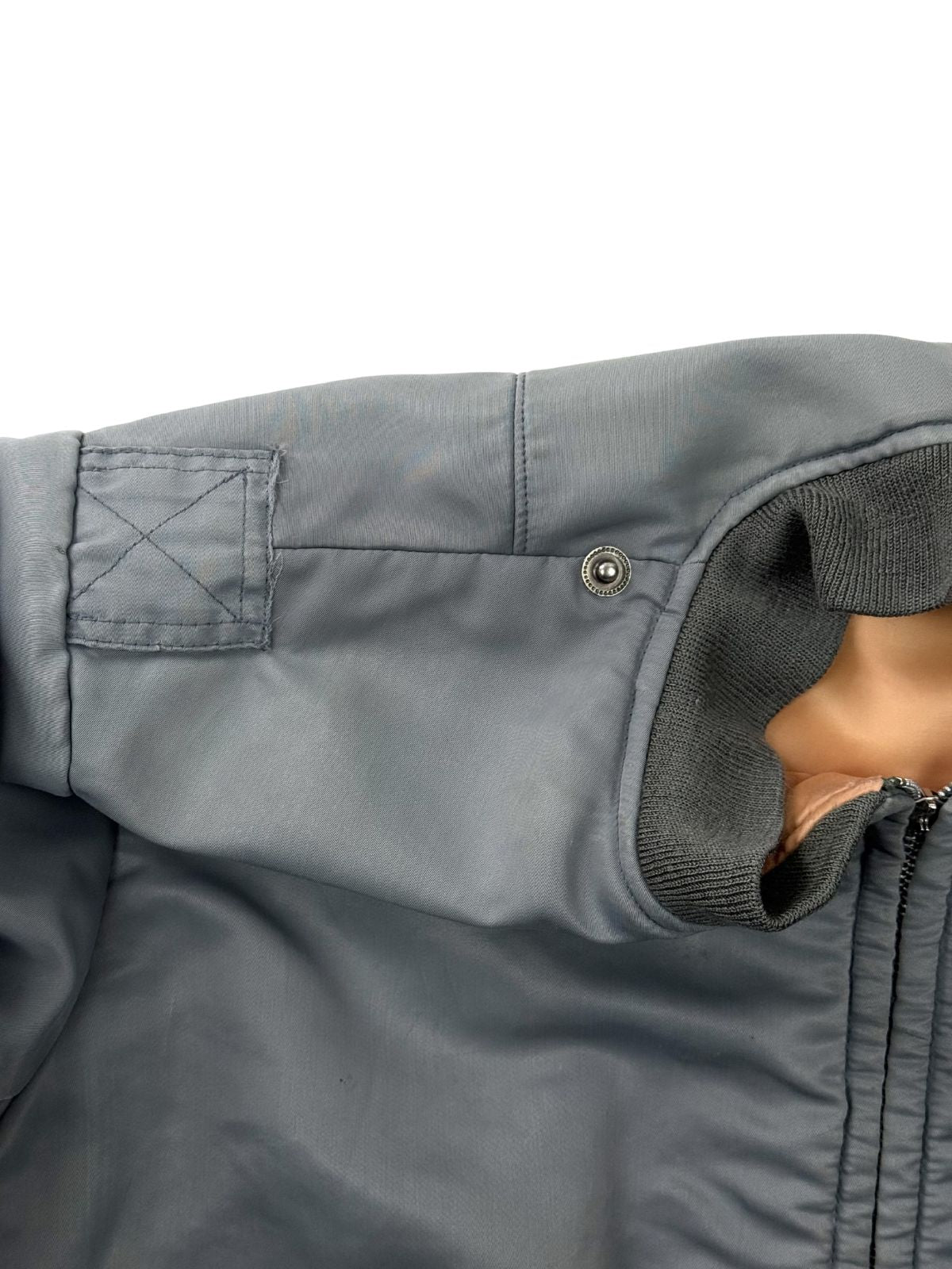 Nahaufnahme der rechten Schulterpartie; zeigt die markanten Nahtspuren und Verstärkungen einer entfernten Schulterklappe auf dem silbrig-blauen Nylon.