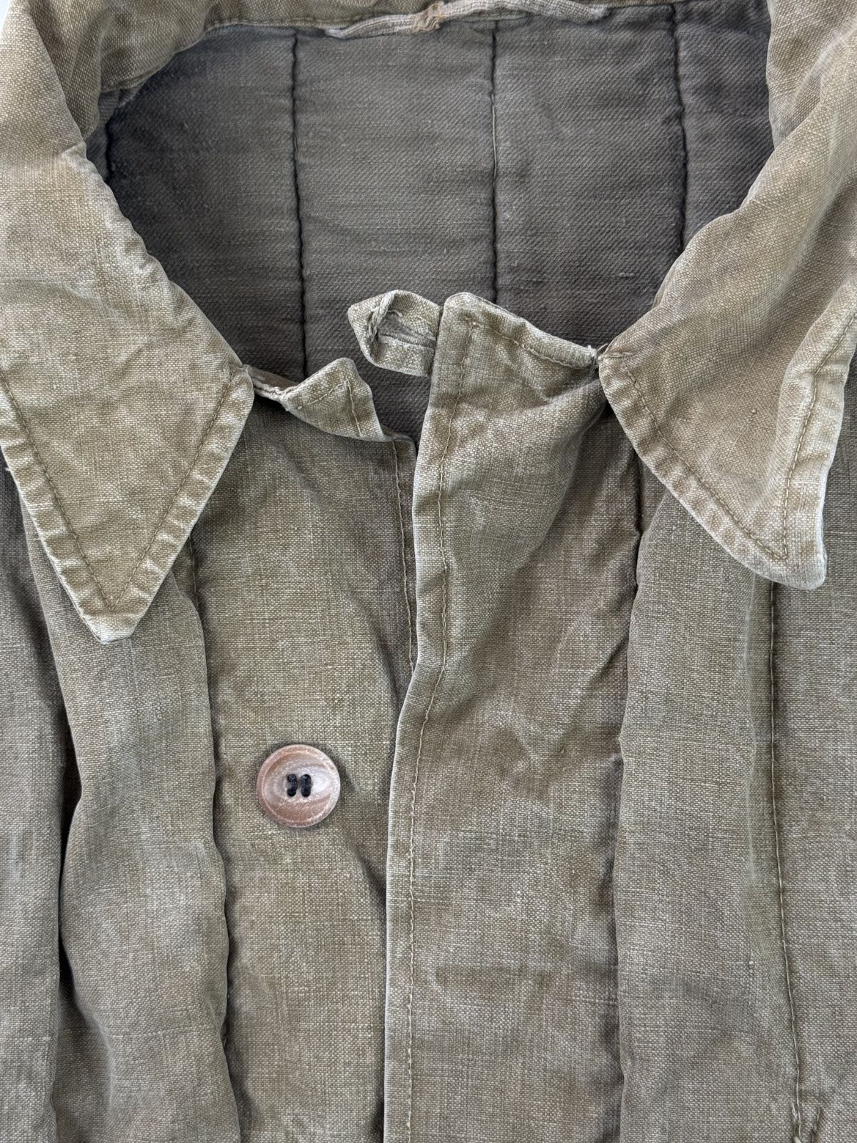 Nahaufnahme des Kragensystems der Telogreika-Jacke mit Fokus auf die feste Stoffstruktur, eine kleine Gewebeschlaufe am Halsansatz und die handvernähten Knopflöcher.
