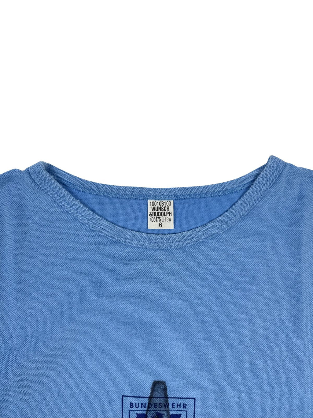 Nahaufnahme des Nackenetiketts: Weißes Etikett des Herstellers „WUNSCH RUDOLPH“, Größe 6, eingenäht in den hellblauen T-Shirt-Kragen.