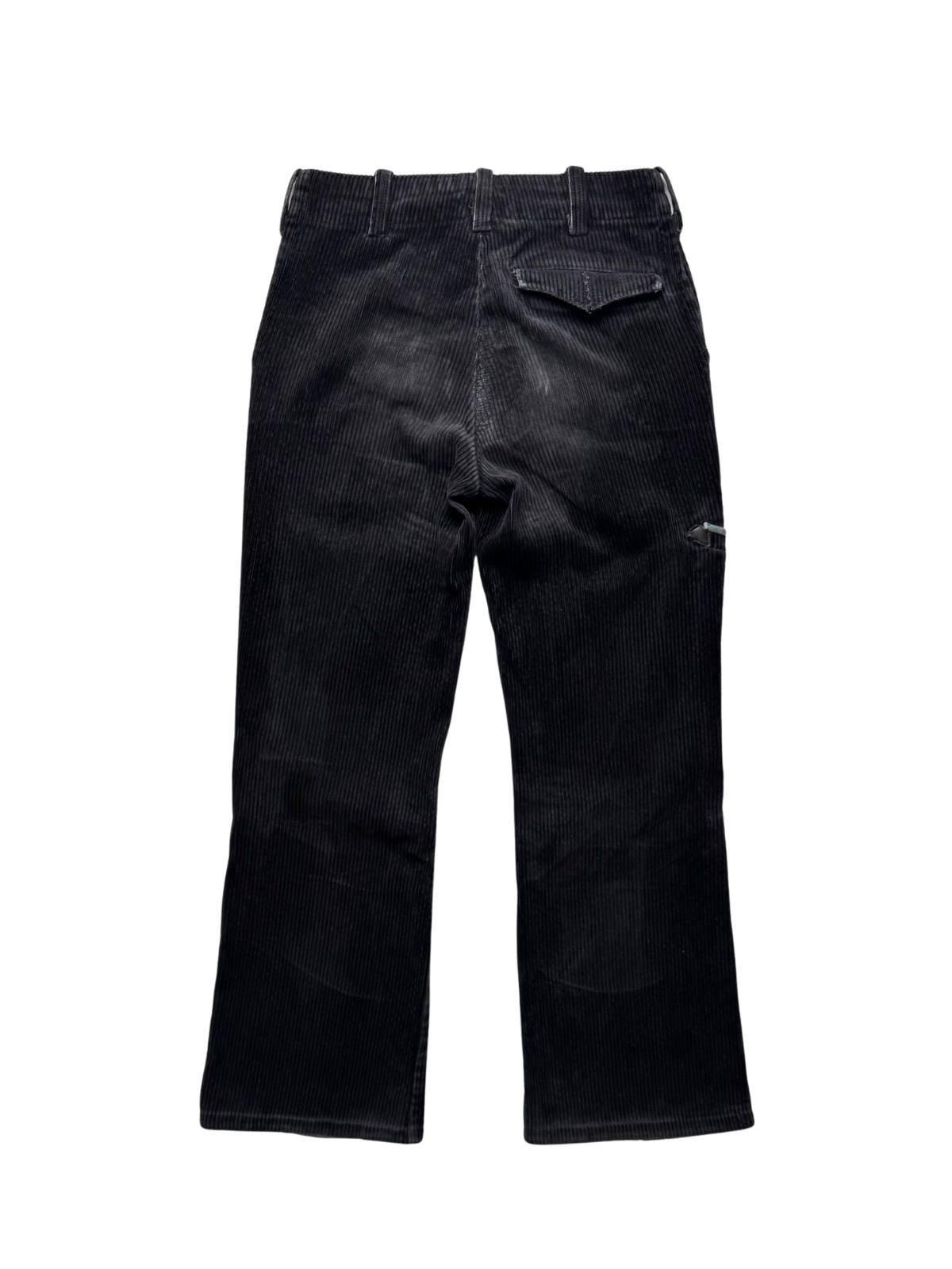 Rückseite der schwarzen Cord-Zunfthose in der Gesamtansicht mit Gürtelschlaufen, geknöpfter Gesäßtasche mit Patte und leicht ausgewaschenen Abnutzungsspuren im Gesäßbereich.