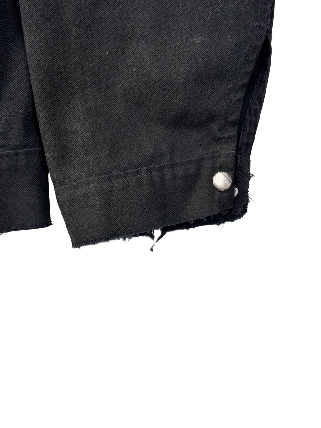Makroaufnahme des linken Handgelenks; zeigt den ausgefransten Saum (Fraying) und den Metalldruckknopf der Arbeitsjacke.