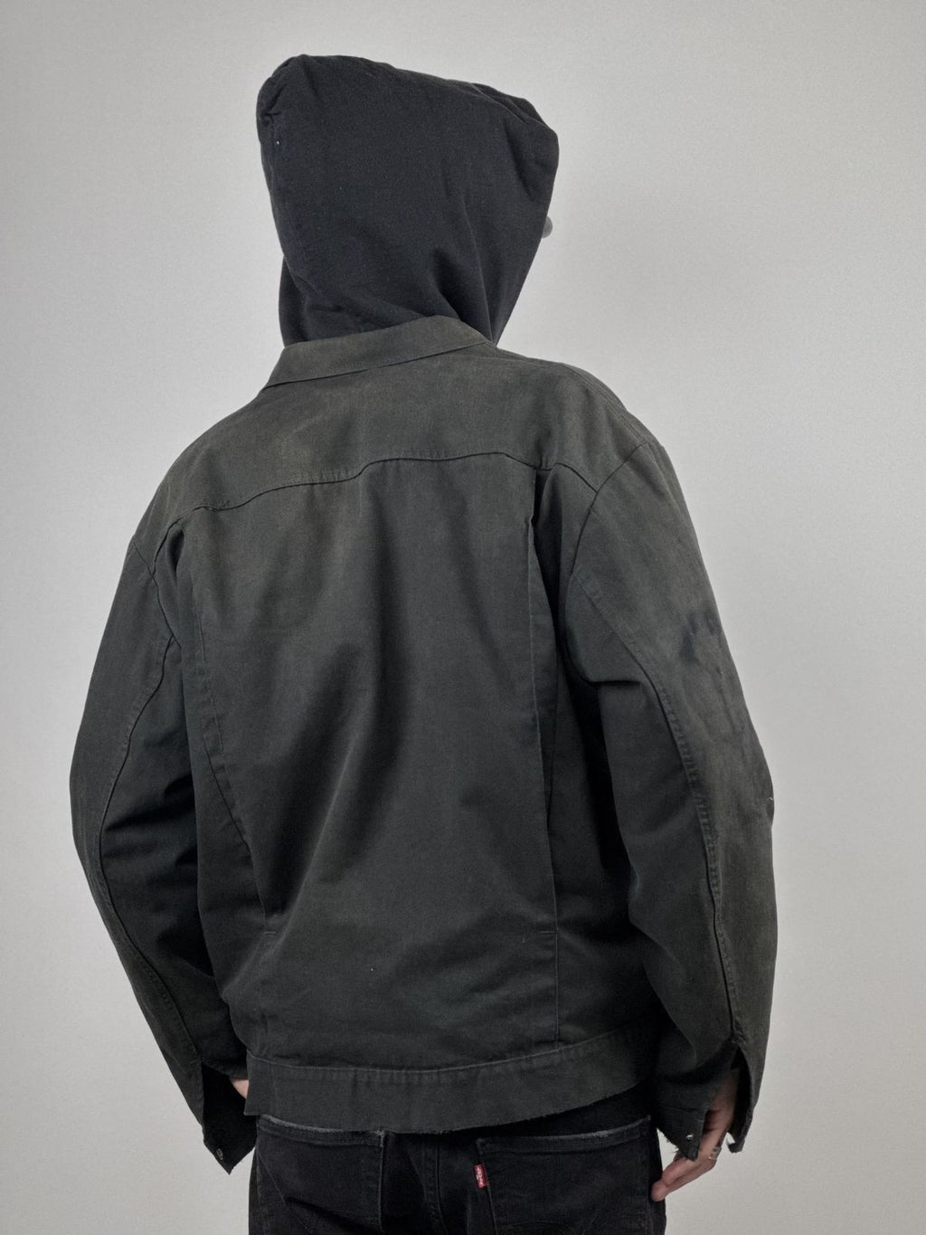 Rückseite des Models in der distressed Workwear Jacke; verdeutlicht den kurzen Schnitt und den Sitz der Schulterpartie.