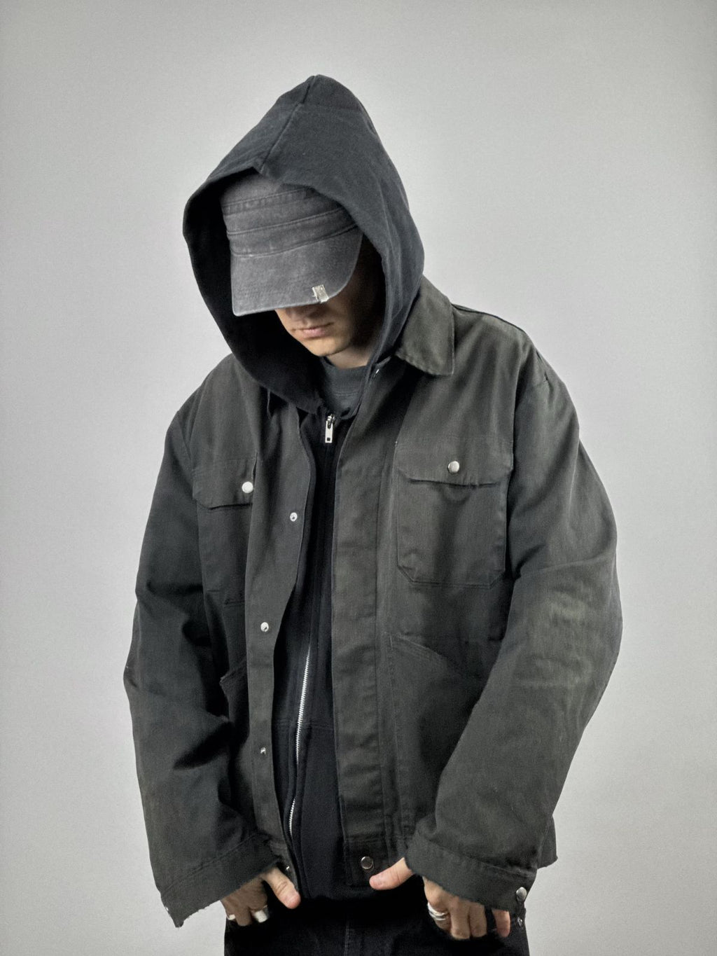 Model trägt die verwaschene Arbeitsjacke über einem schwarzen Hoodie; zeigt die weite Passform und den robusten Streetwear-Look.