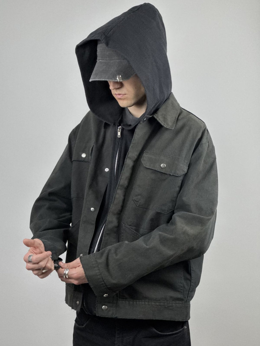 Model trägt die verwaschene Arbeitsjacke über einem schwarzen Hoodie mit schwarzer Mütze; zeigt die weite Passform und den robusten Streetwear-Look.