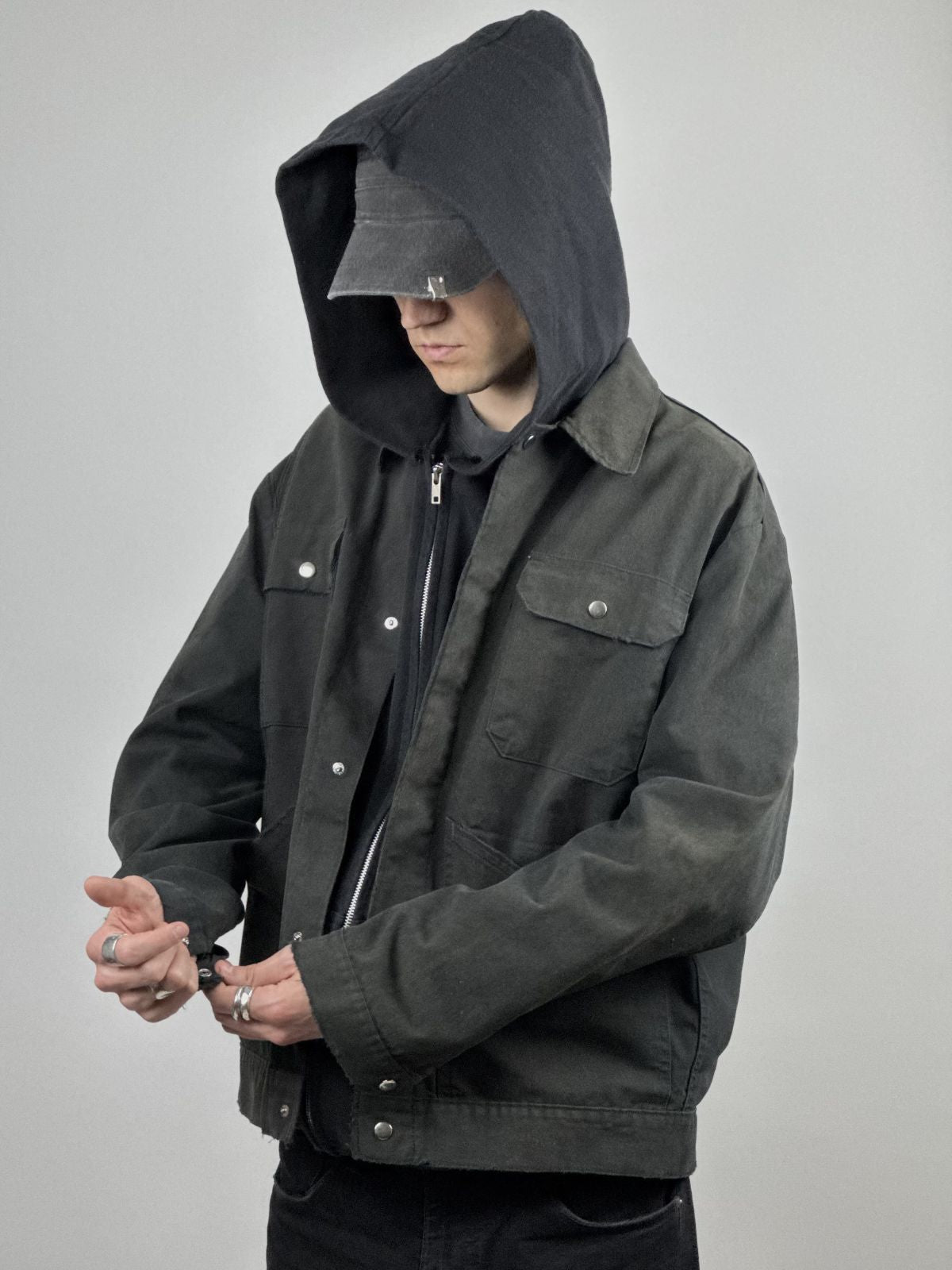 Model trägt die verwaschene Arbeitsjacke über einem schwarzen Hoodie mit schwarzer Mütze; zeigt die weite Passform und den robusten Streetwear-Look.