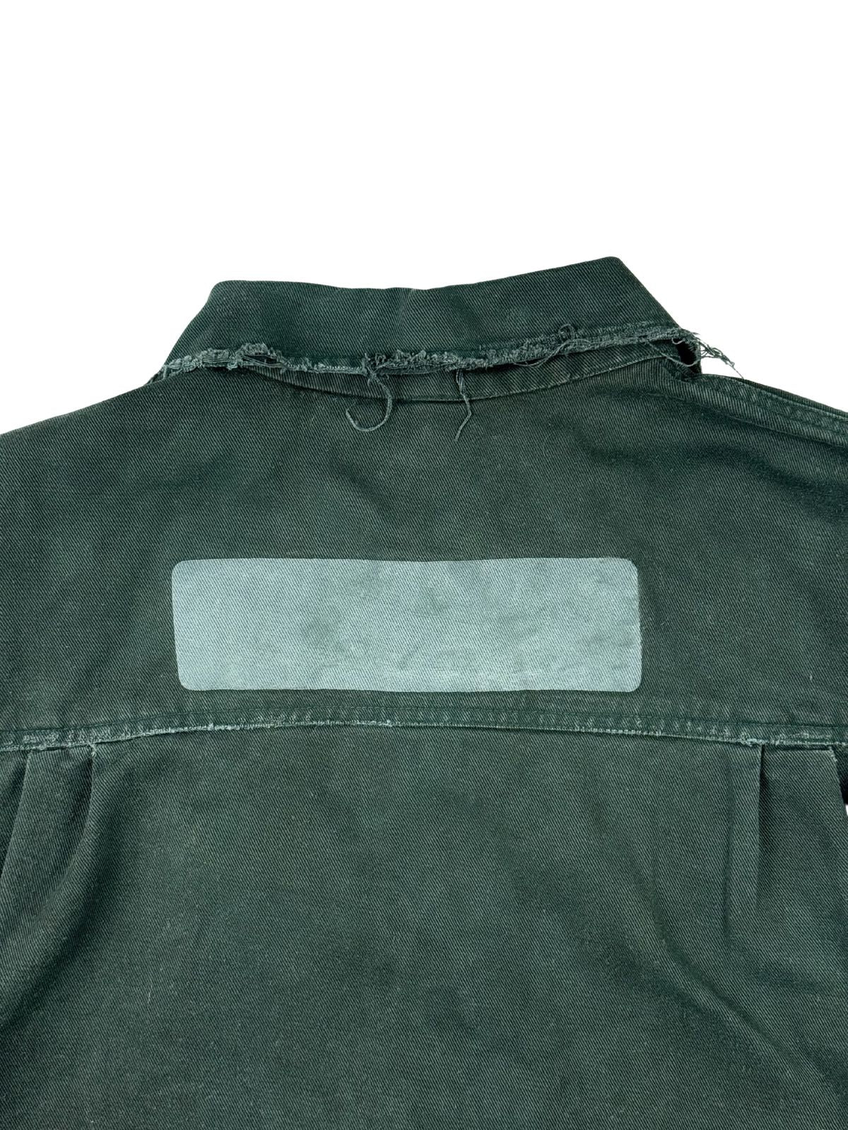 Nahaufnahme der oberen Rückseite mit Fokus auf den stark ausgefransten Kragenrand (Fraying) und den kontrastierenden, rechteckigen Abdruck eines entfernten Aufwind-Patches.