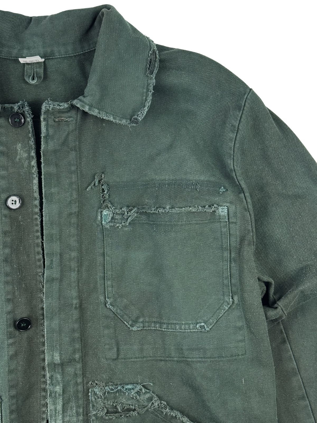 Detailaufnahme der vorderen linken Brusttasche, deren offene Stoffkante stark zerschlissen und ausgefranst ist.
