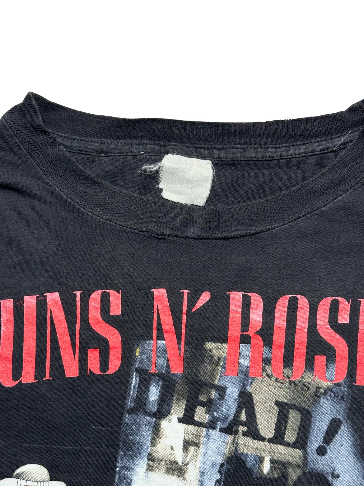 Detailansicht der vorderen Brustpartie mit geripptem Rundhalsausschnitt, dem roten „GUNS N’ ROSES“-Schriftzug und dem verwaschenen Stoffetikett.