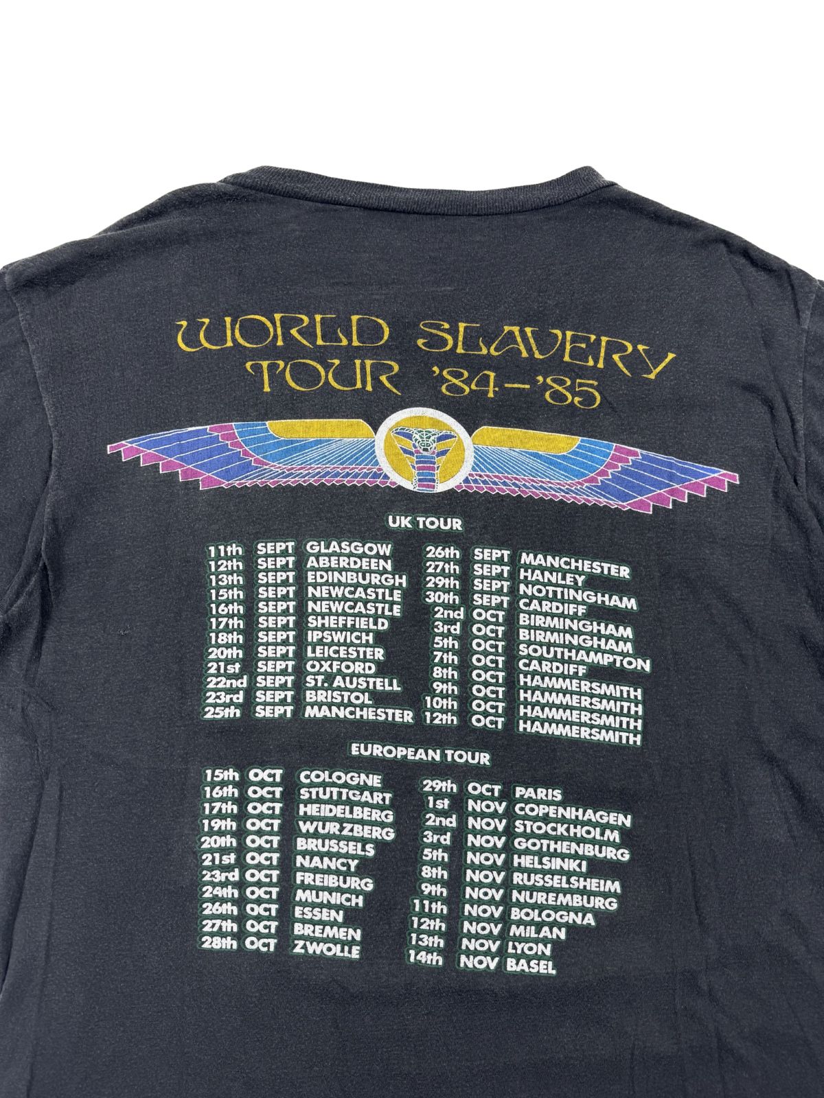 Nahaufnahme der Rückseite eines Iron Maiden World Slavery Tour Shirts; zeigt die Liste der Tourdaten 1984 für UK und Europa unter dem geflügelten Skarabäus-Logo.