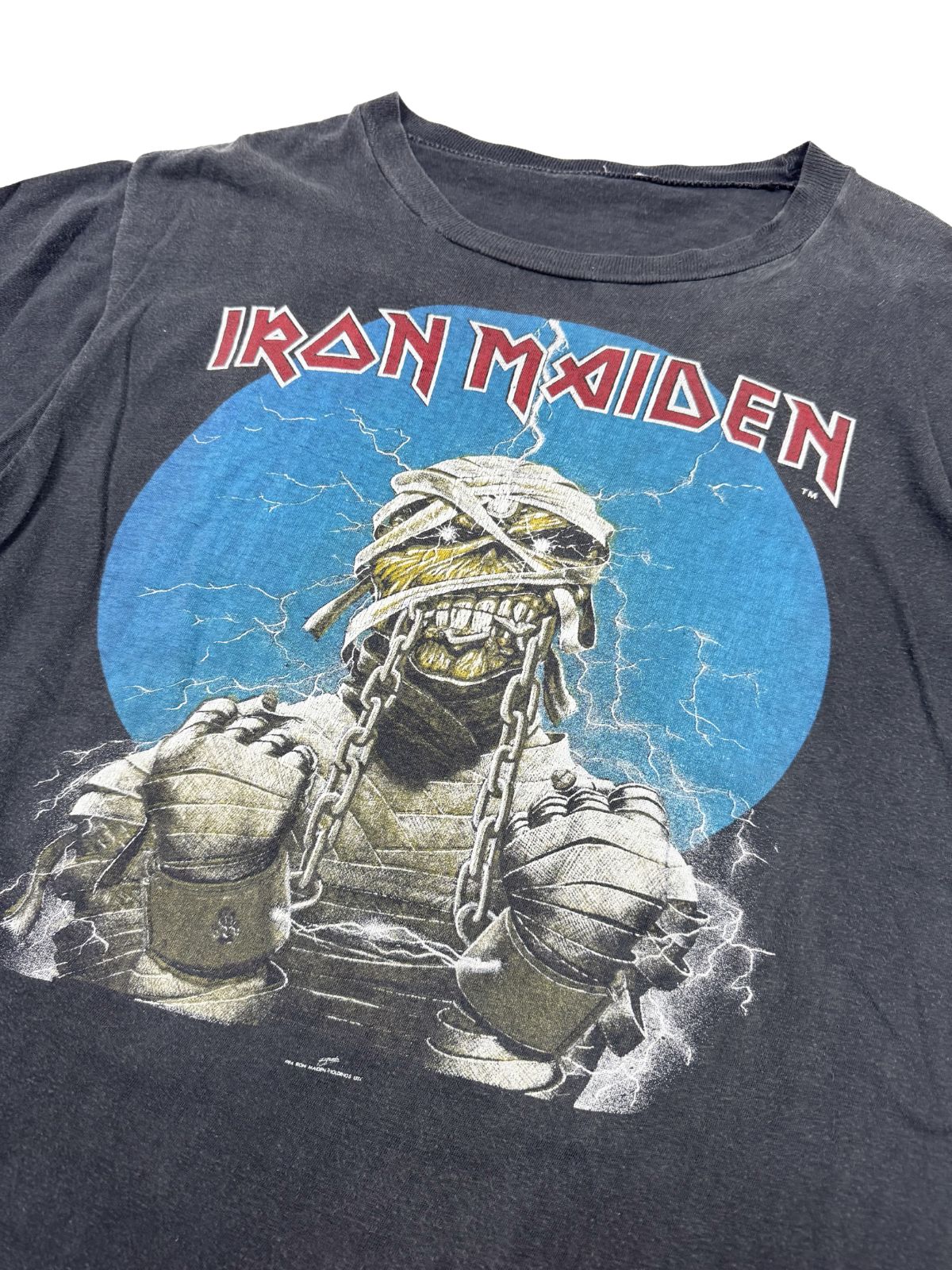 Nahaufnahme der Vorderseite des Iron Maiden Powerslave Shirts; zeigt Eddie als Mumie in Ketten vor einem blauen Kreis mit Blitzen.