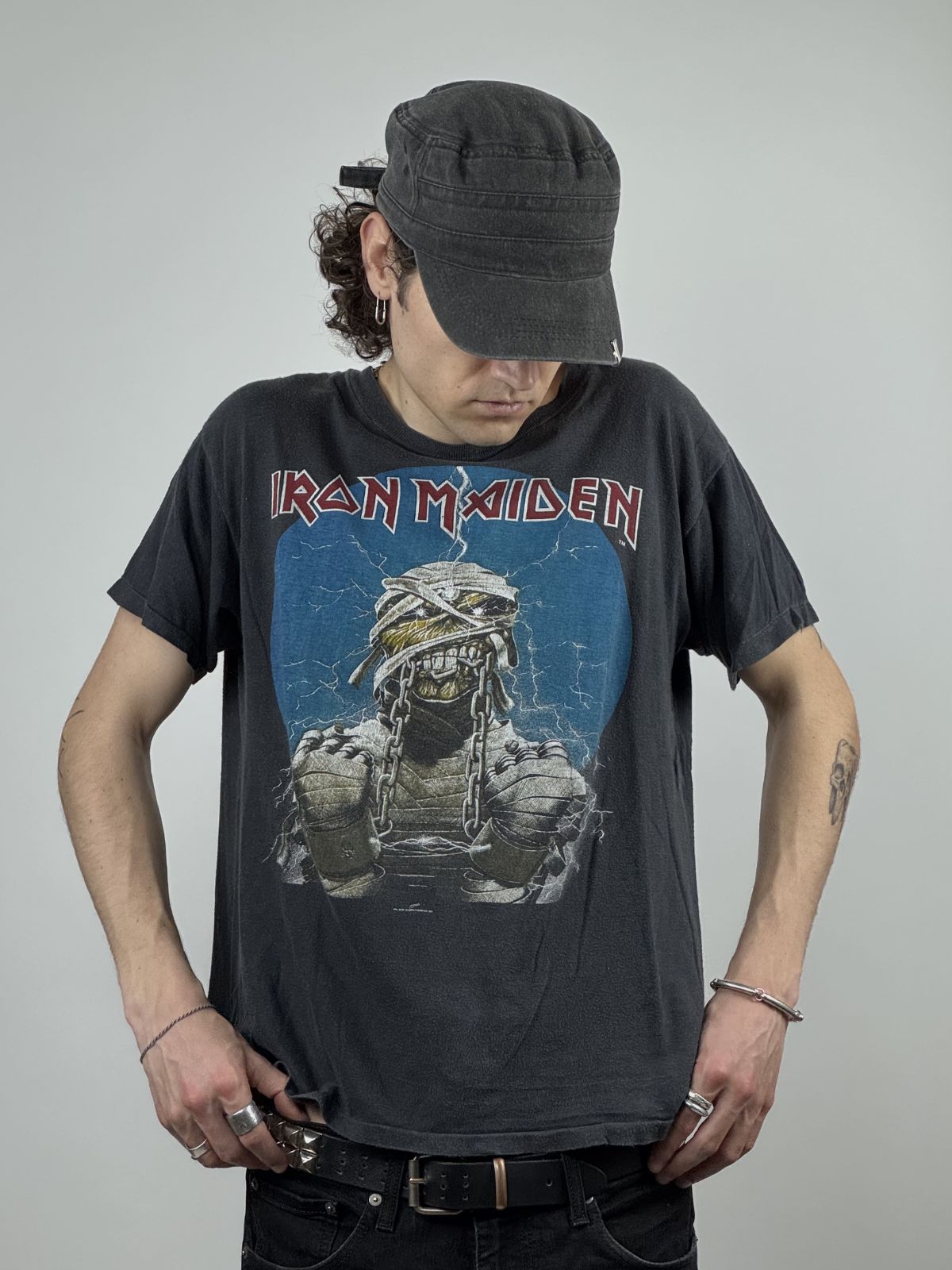 Ein Model trägt das Iron Maiden Powerslave Vintage Shirt kombiniert mit einer Schirmmütze und Nieten-Accessoires im Rock-Look.