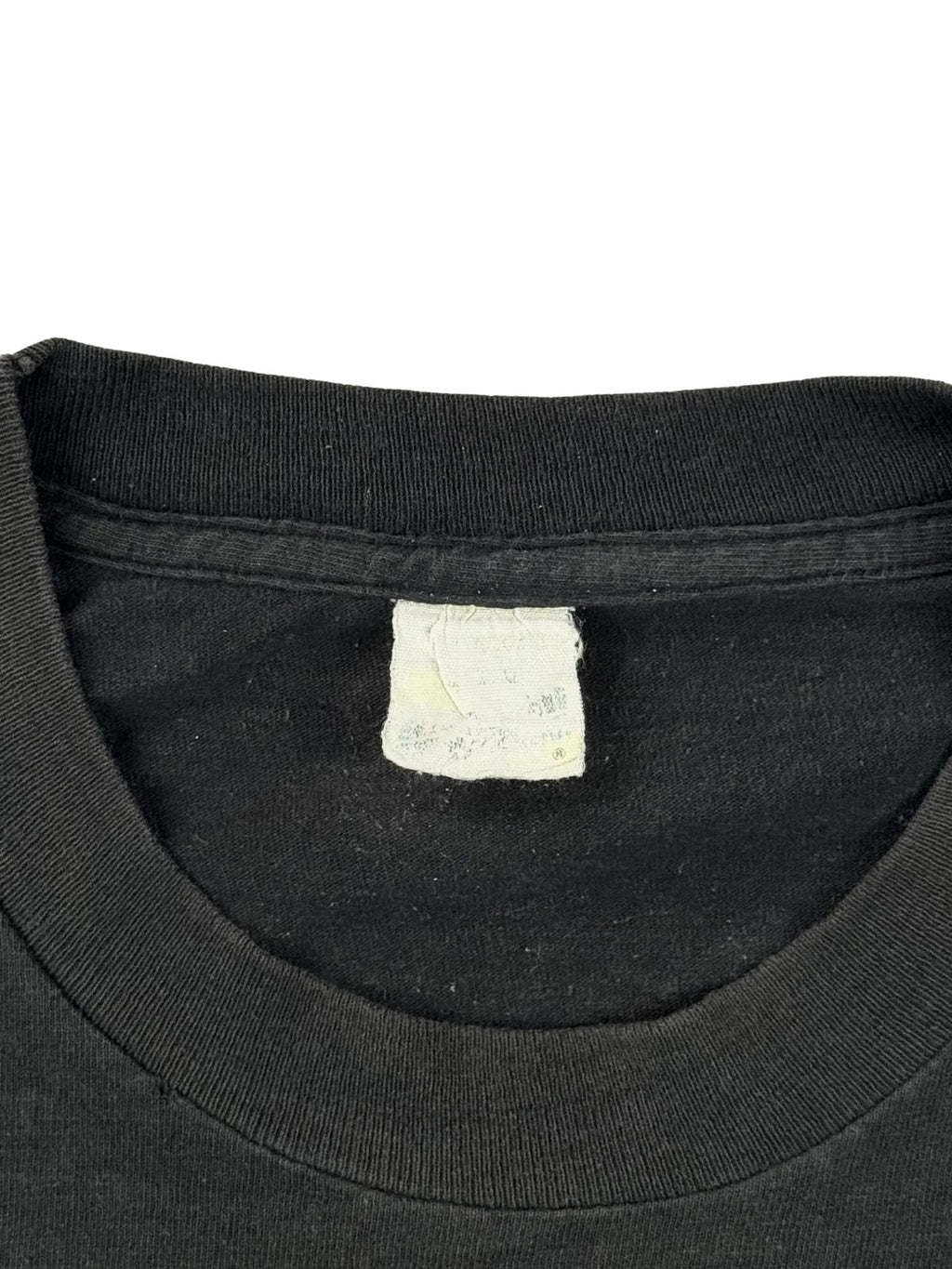 Nahaufnahme des Halsausschnitts und des stark verwaschenen, weißen Nackenetiketts (Neck Tag) im Kragen des Iron Maiden Shirts von 1988. Ein wichtiges Zustandsdetail, das die jahrzehntealte Alterung und den authentischen Tragecharakter des Vintage-Textils zeigt.