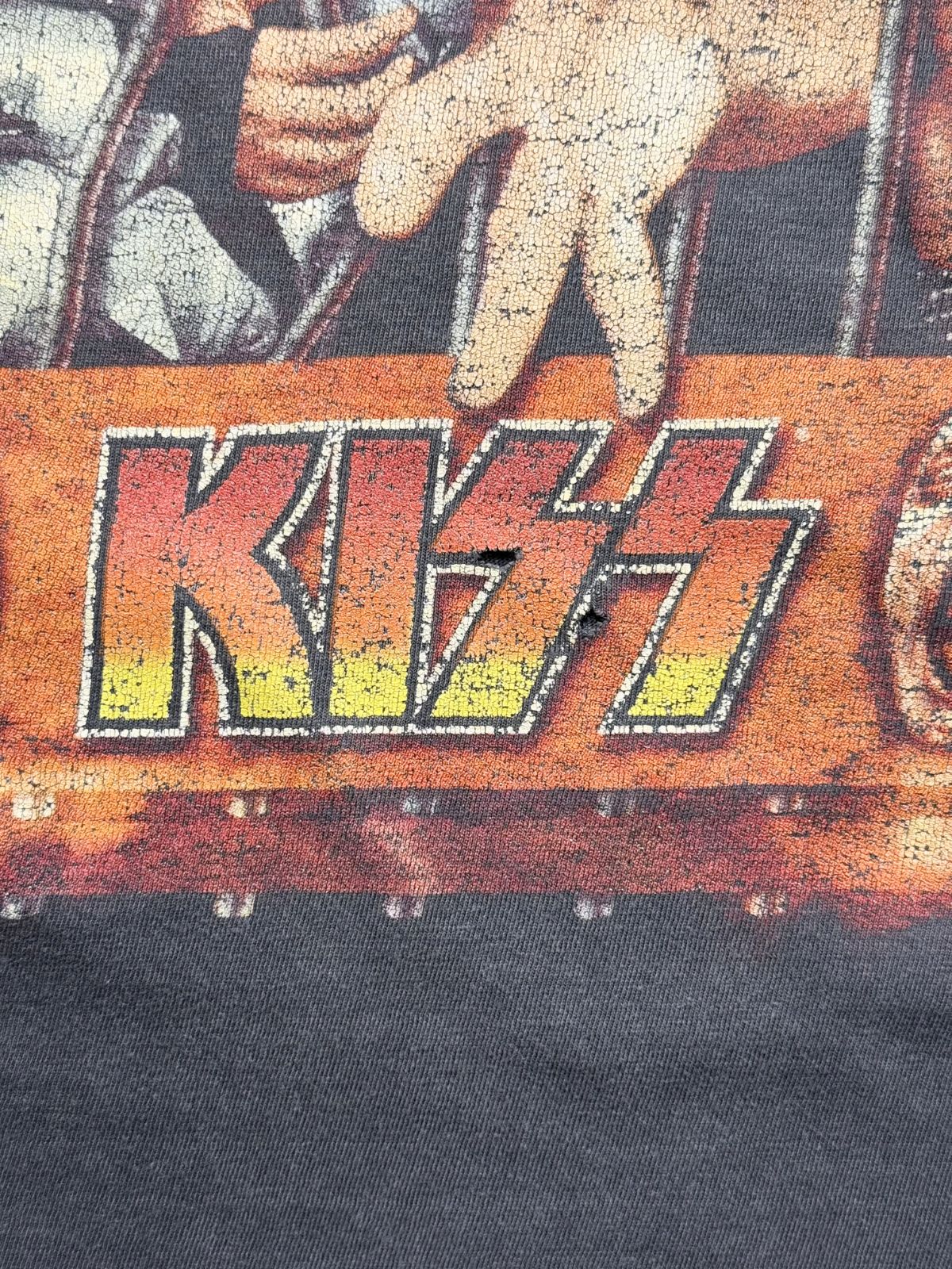 Detailaufnahme des Frontprints mit Fokus auf zwei kleine Löcher (Pinholes) direkt im gelb-roten „KISS“-Schriftzug zur genauen Zustandsdokumentation.