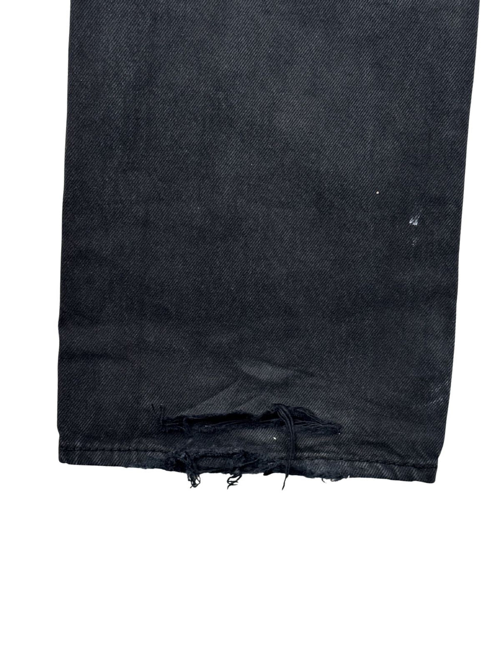 Detailaufnahme des linken Hosenbeins einer schwarzen Levi's 501 Vintage Jeans mit ausgefranstem Saum und Heel-Bite-Abnutzung.