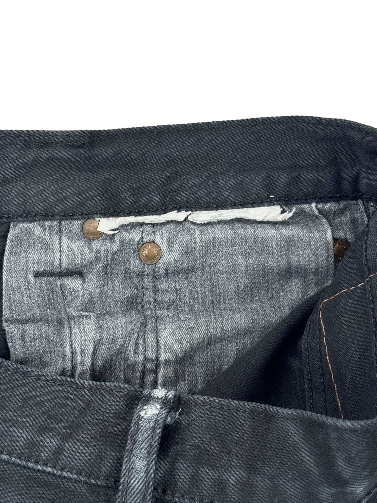 Detailansicht des inneren Hosenbunds einer schwarzen Vintage Levi's Jeans mit kupferfarbenen Nieten und Resten eines entfernten Etiketts.